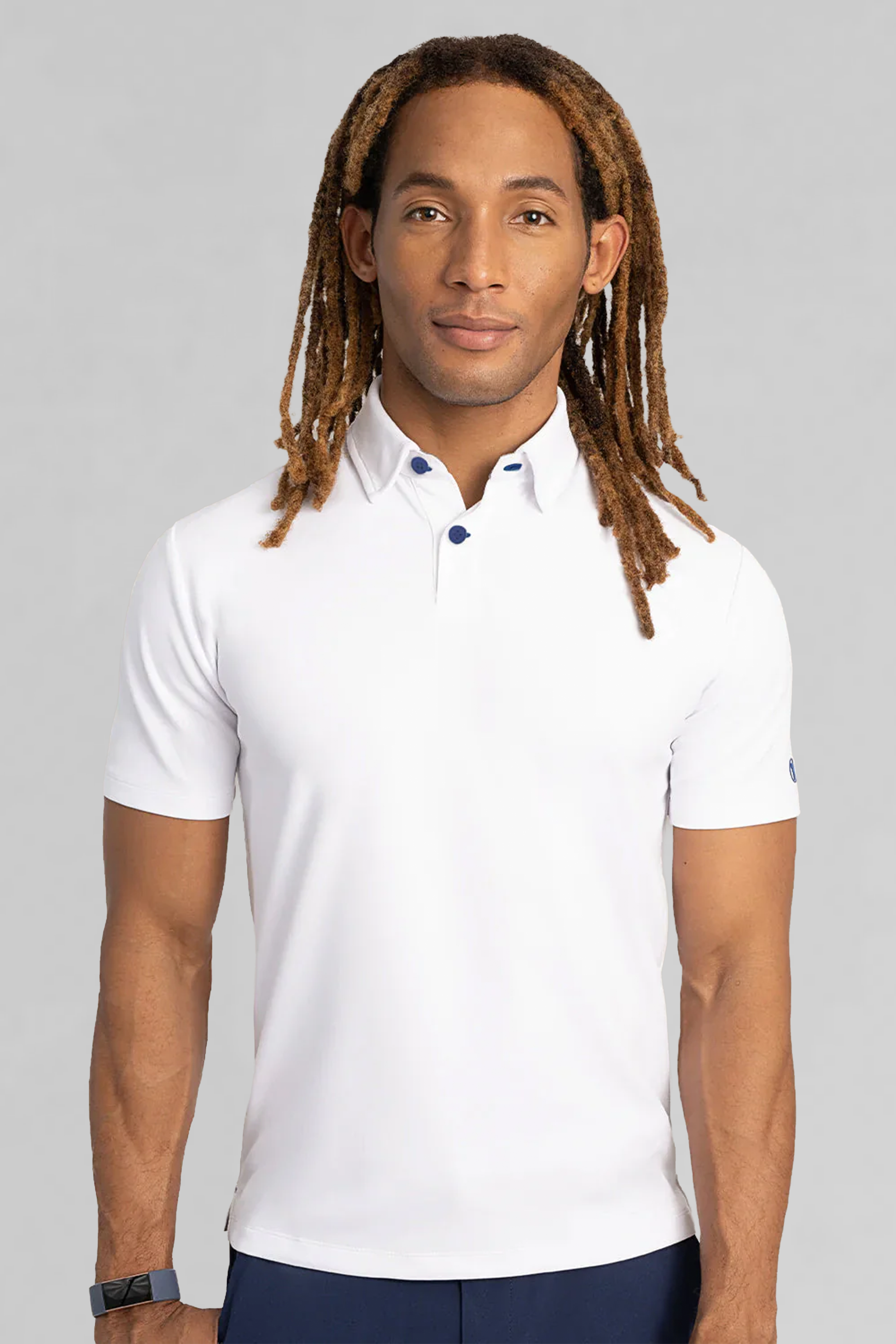 A person with long, light brown dreadlocks wears the Twillory Short Sleeve Polo Contrast in White Blue, featuring blue buttons. They stand against a plain light gray background, with a neutral expression and a watch on their left wrist.