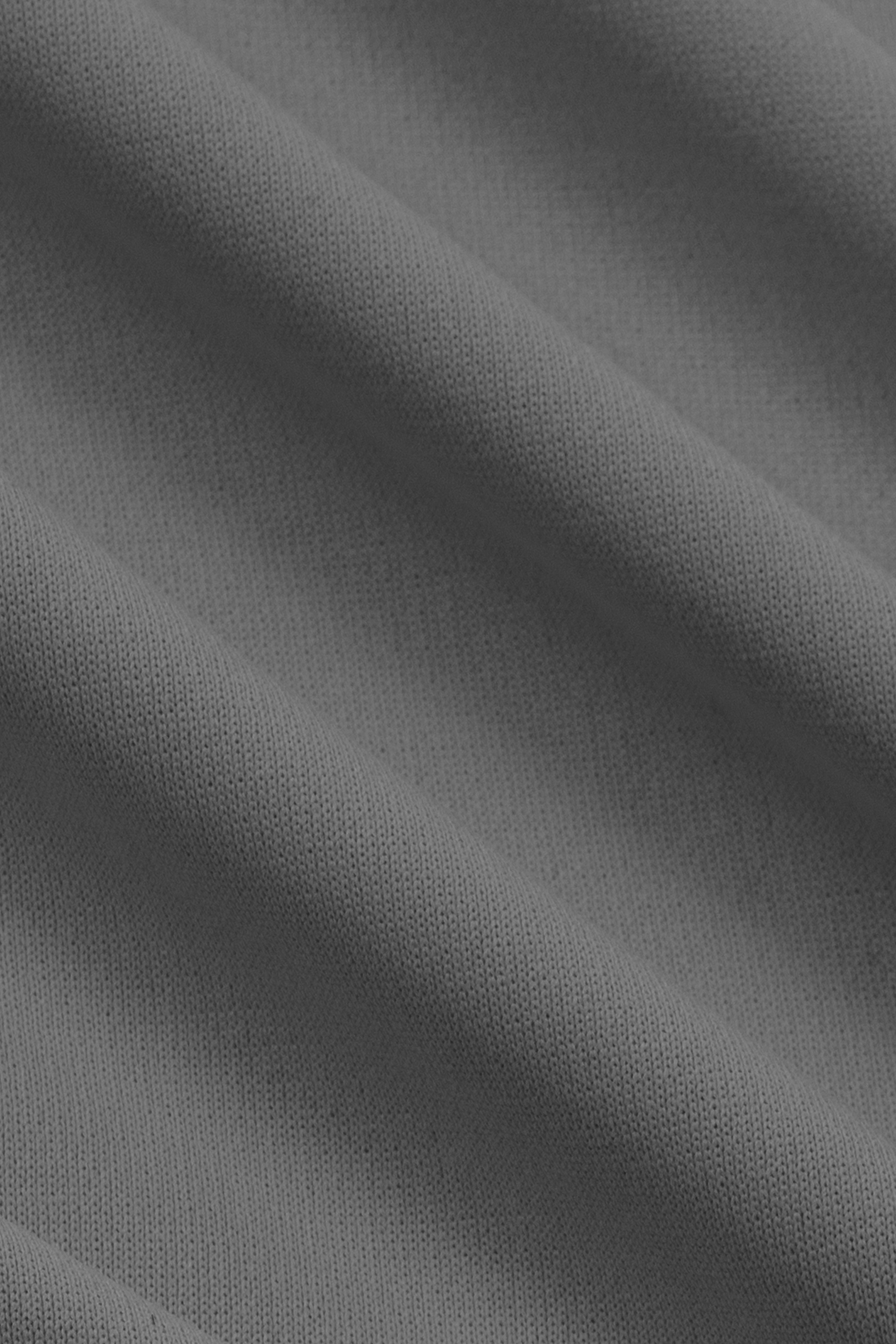 A close-up of the charcoal Short Sleeve Polo Solid by Twillory shows its soft, lightly textured performance fabric. Gentle diagonal folds highlight its smooth, wrinkle-free weave for a flexible, comfortable fit.