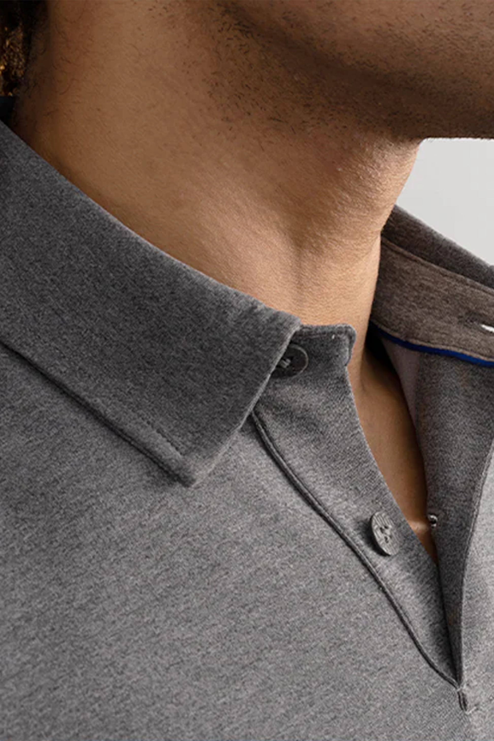 Close-up of a person’s neck and lower face wearing Twillory’s Short Sleeve Polo Solid in Charcoal, featuring a structured collar, two buttons, and soft, textured moisture-wicking fabric. Background is neutral and out of focus.