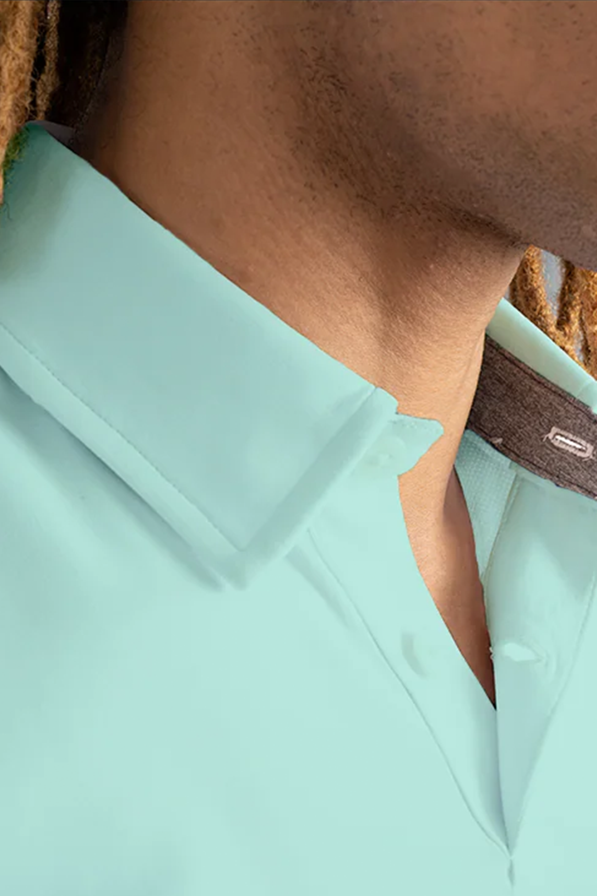 Close-up of a person’s neck and shoulder wearing the Twillory Short Sleeve Polo Solid in Turquoise. The shirt features a structured collar with a visible top button. Brown dreadlocks are visible; the background is blurred.
