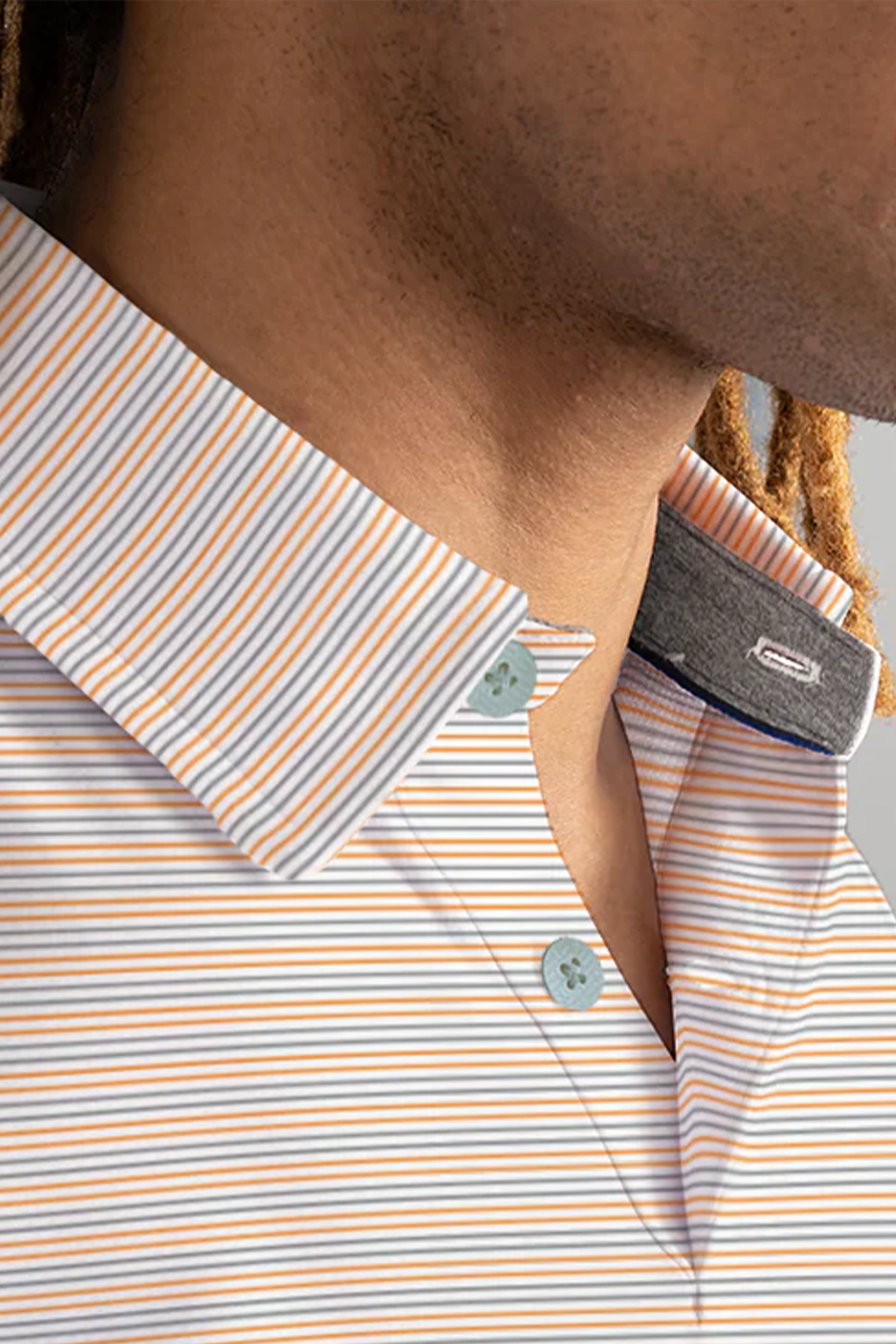 Close-up of a person’s neck and chin wearing Twillory’s Short Sleeve Polo Stripe // Grey Orange, featuring thin white, orange, and blue stripes, stretch fabric, two light blue buttons, a dark inner collar detail, and visible dreadlocks.