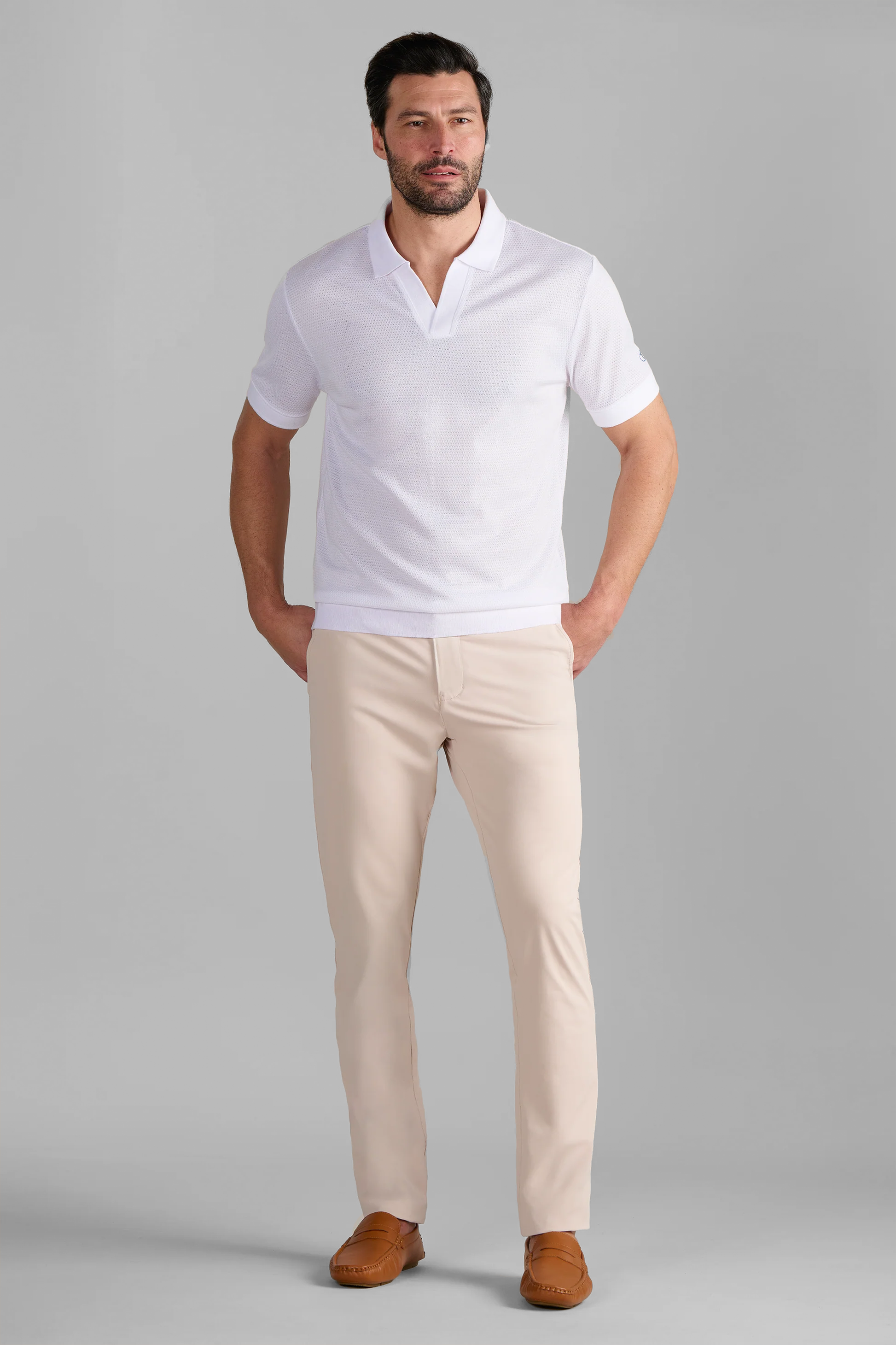 A man wears the Twillory Short Sleeve Sweater Polo Solid in white with beige pants, showcasing comfortable, wrinkle-free performance fabric.