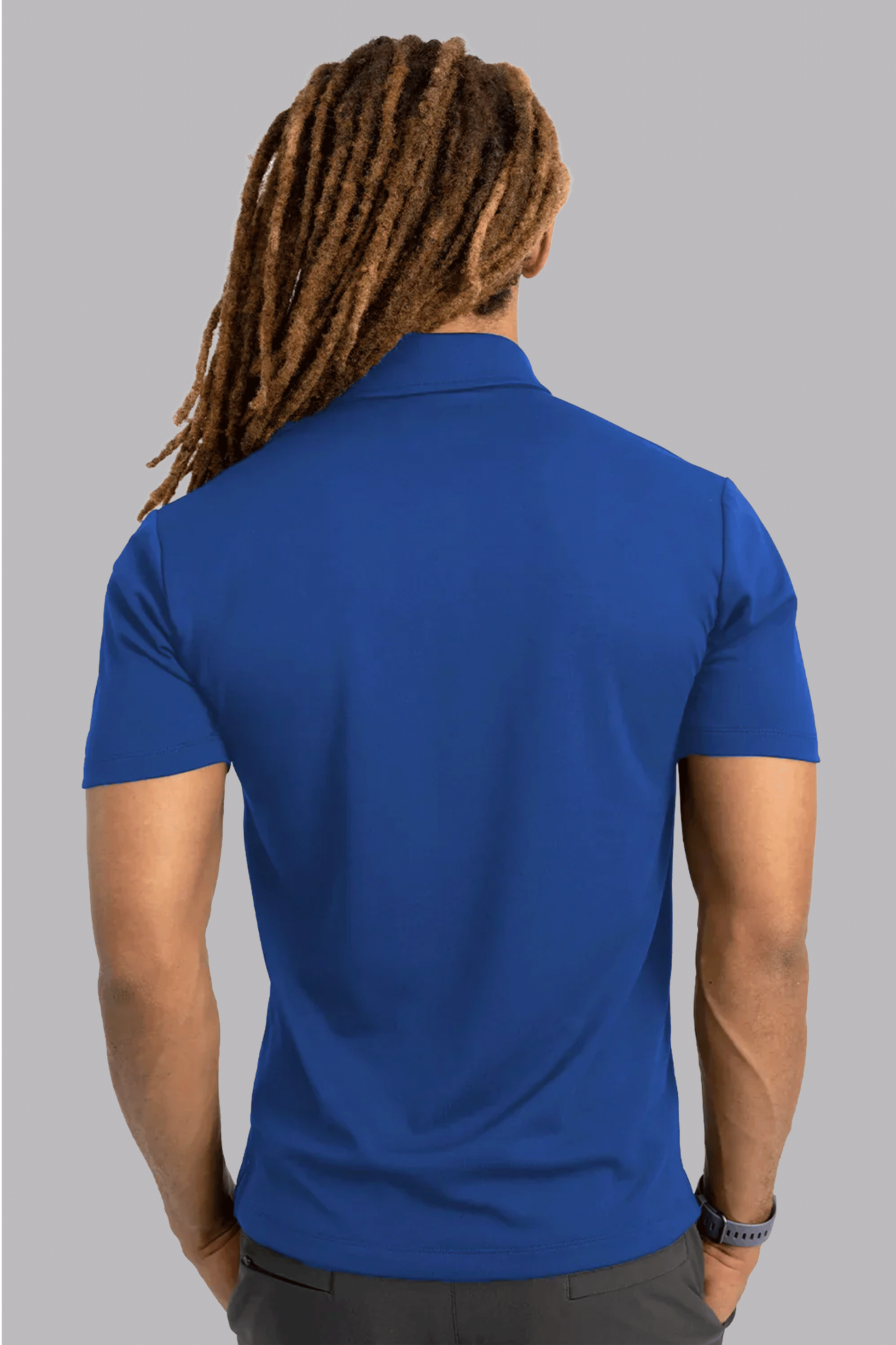 A person with long, brown dreadlocks is shown from the back, arms relaxed by their sides, wearing a Twillory Short Sleeve Polo Solid in Twilight and dark pants against a plain light gray background.