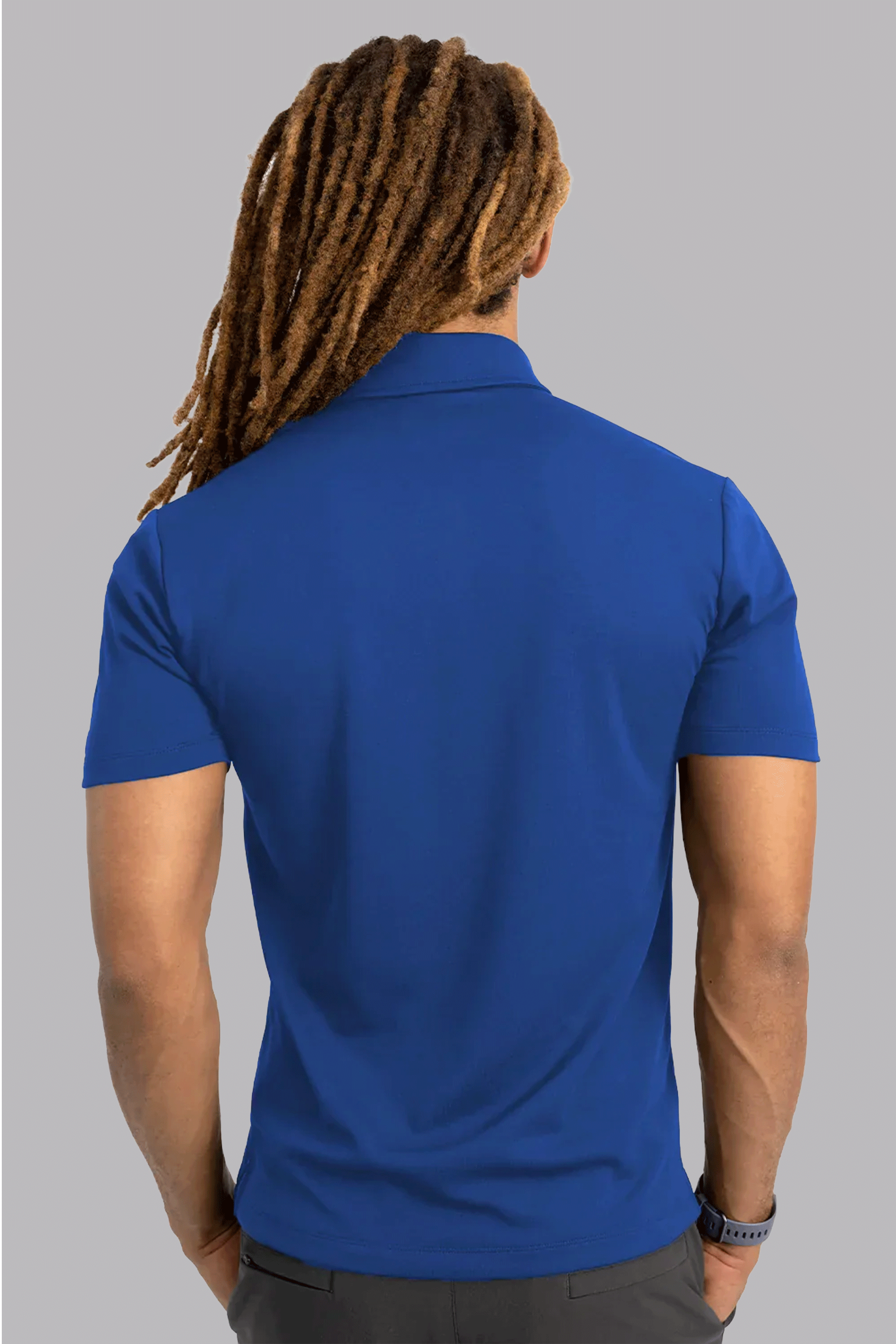 A person with long, brown dreadlocks is shown from the back, arms relaxed by their sides, wearing a Twillory Short Sleeve Polo Solid in Twilight and dark pants against a plain light gray background.