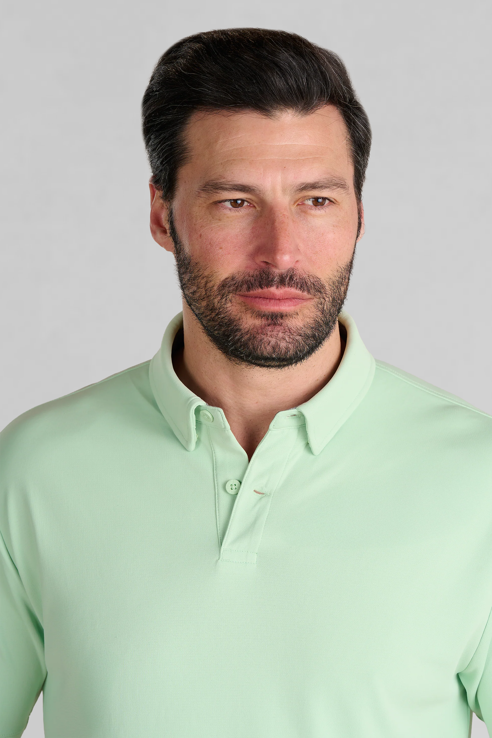 A man with dark hair and a beard wears the Twillory Short Sleeve Polo Solid in Pastel Green. He looks slightly right with a neutral expression against a plain light gray background.
