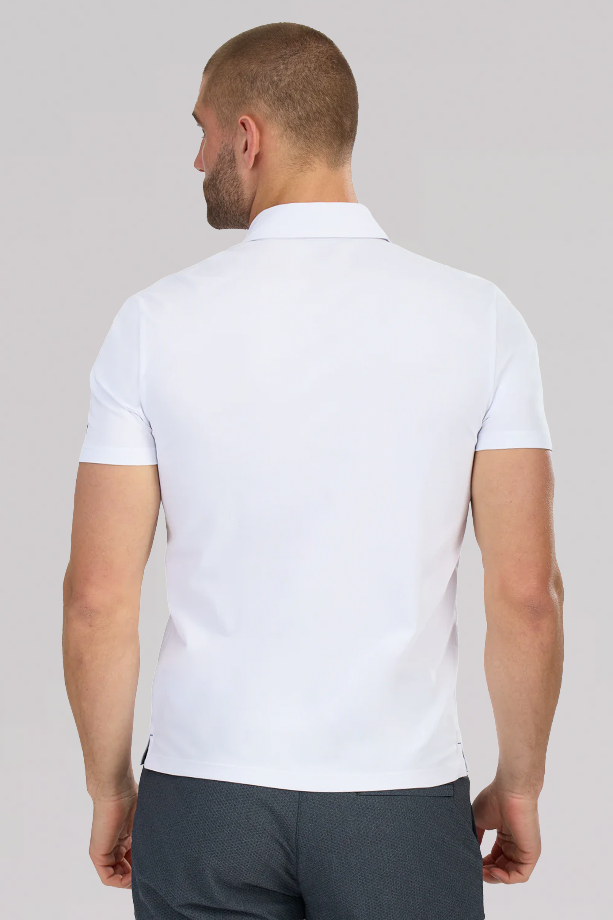 A man with short hair and a beard stands with his back to the camera, wearing the Twillory Slim Fit Pique Polo Contrast in white blue and dark gray pants against a plain light gray background.