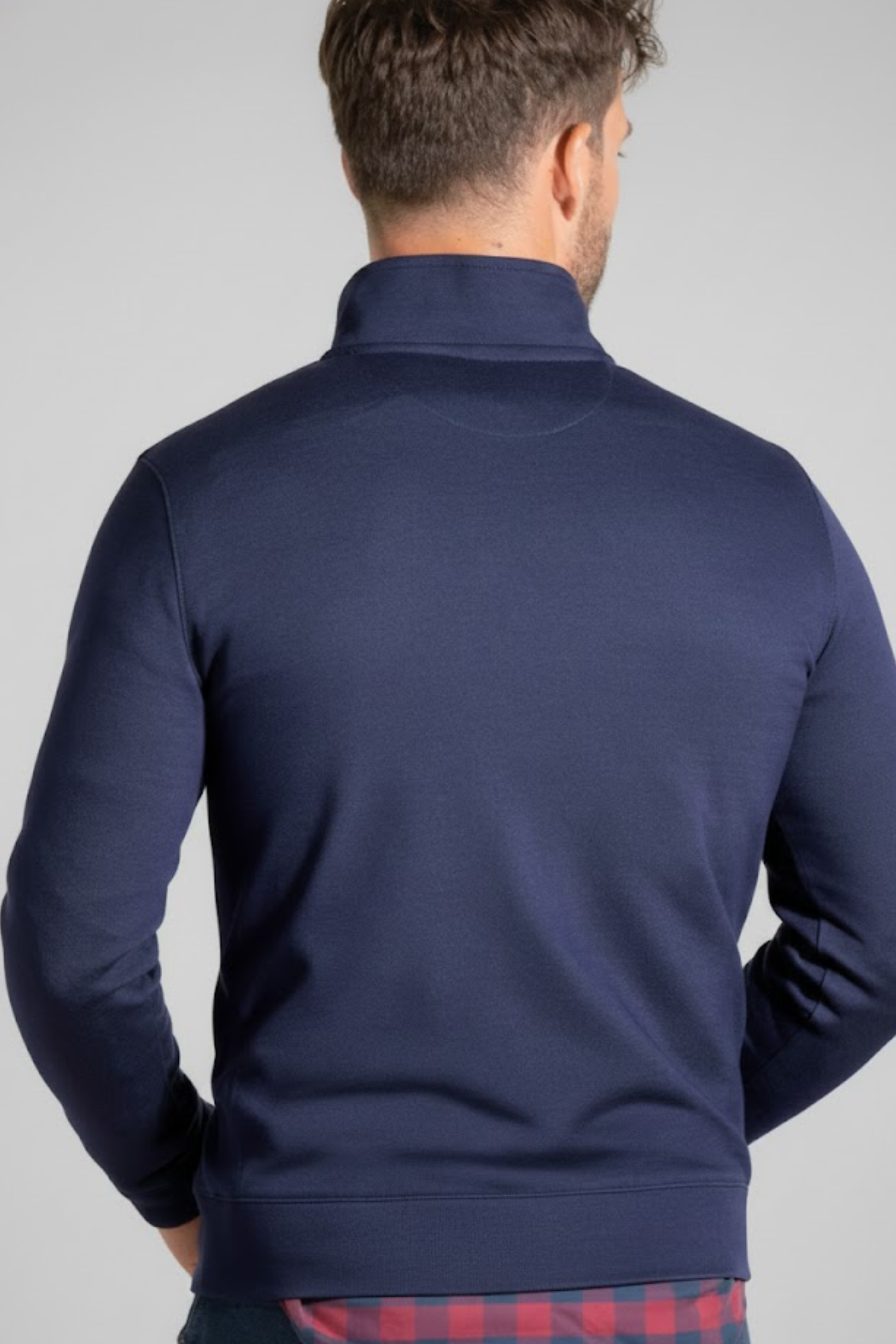 A man with short brown hair is seen from behind wearing the Twillory Performance Quarter Zip // Denim jacket with a high collar over a red and blue plaid Twillory shirt, set against a plain light gray background.
