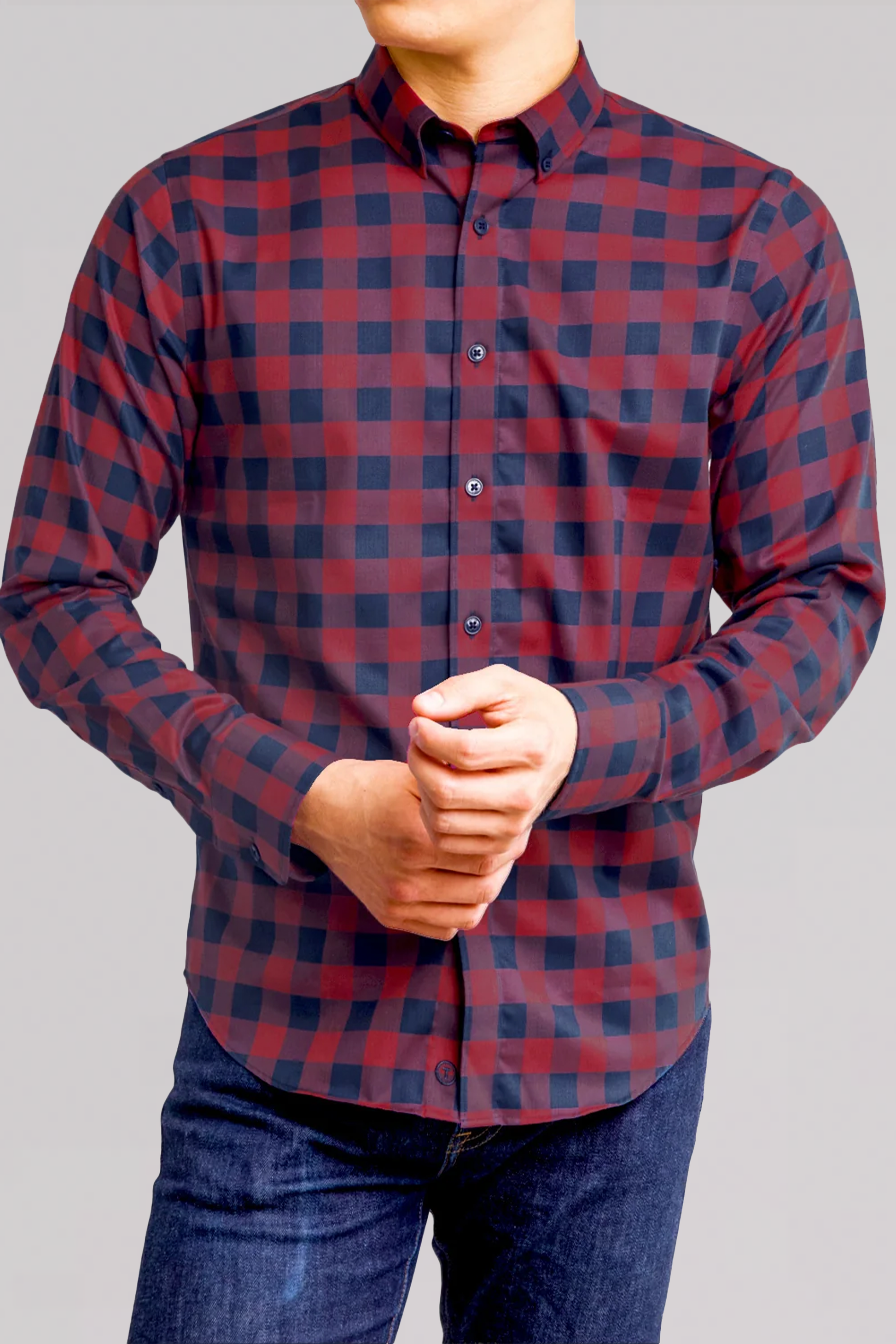 A man wears the Twillory untuck(able) Barnyard Gingham, a smart casual long-sleeved red and navy checkered shirt, paired with dark blue jeans against a plain light gray background; his face is partially turned away.