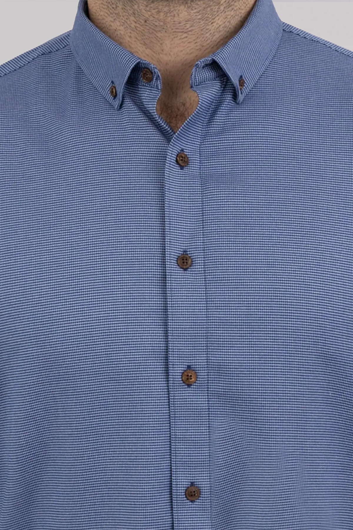 A close-up shows someone wearing Twillory’s untuck(able) Blue Puppytooth shirt with brown buttons and a button-down collar. Only the neck, chest, and upper shirt are visible—face hidden—perfect for smart casual style.
