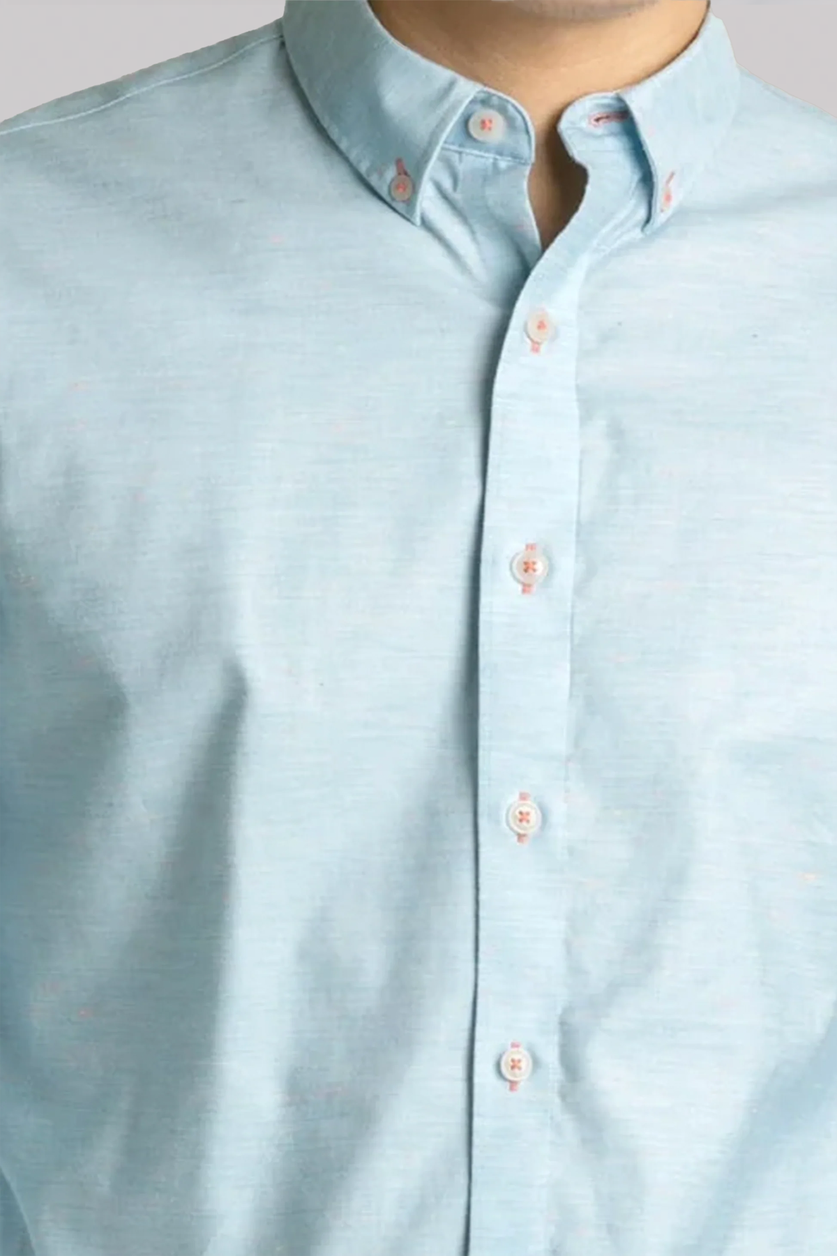 A close-up shows a person wearing the Twillory untuck(able) Caribbean Melange shirt—a light blue non-iron stretch button-down with a classic collar and five white buttons, styled smart-casual against a plain background.