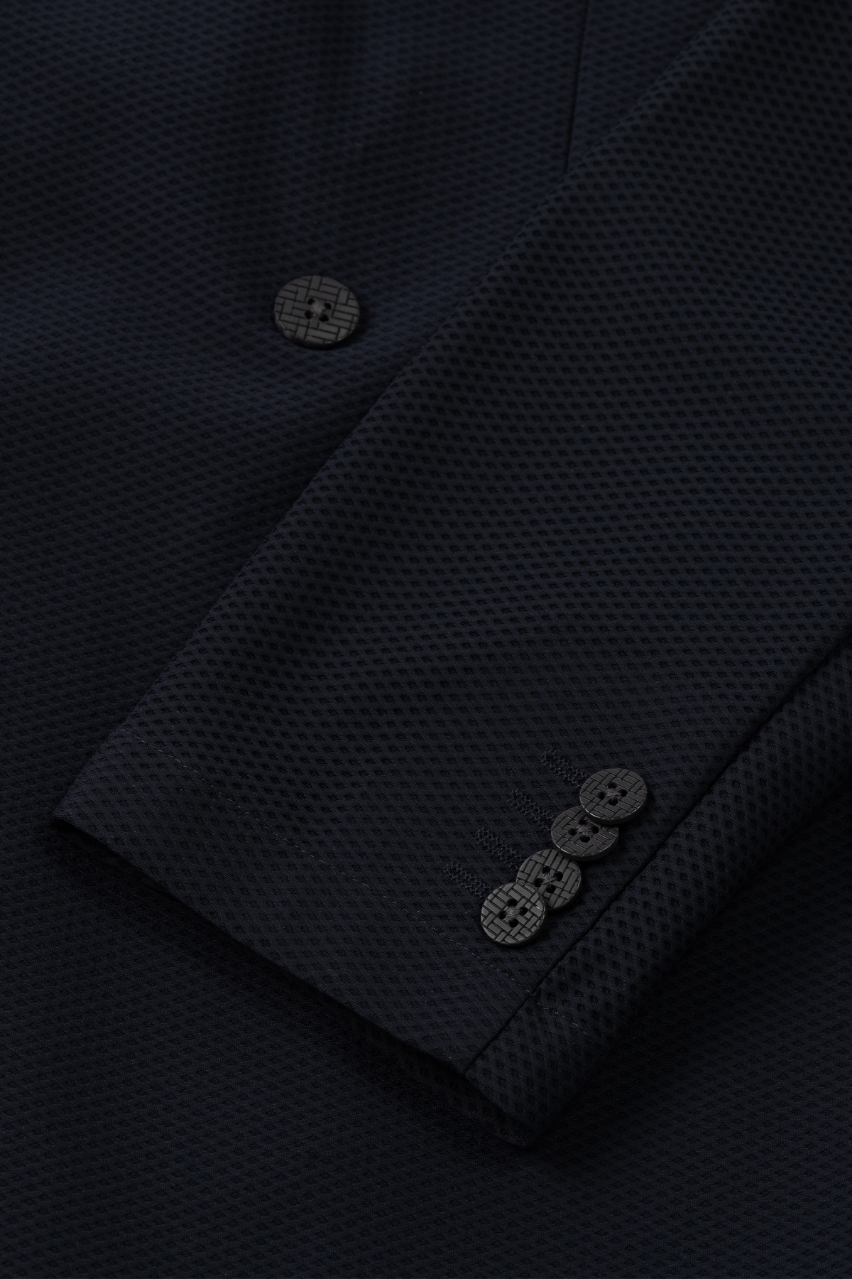 Close-up of the Twillory AIR Double Breasted Blazer // Black sleeve, showing four black cuff buttons. The 360° Airflow Fabric has a subtle dot pattern, highlighting fine detailing and quality stitching on this machine washable blazer.