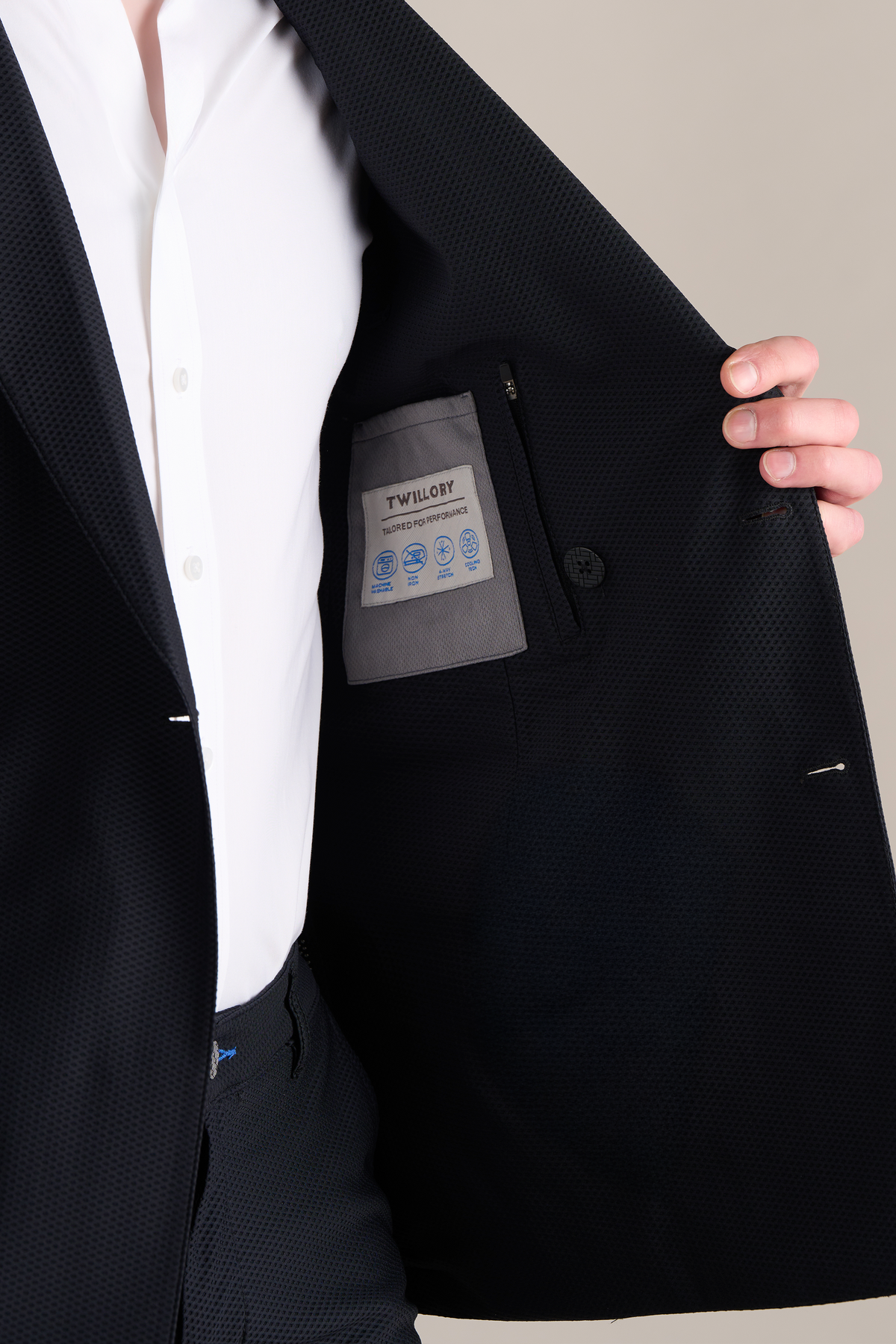 A person in a white shirt opens a Twillory AIR Double Breasted Blazer in black, featuring 360° Airflow Fabric and revealing the light gray inner pocket lining with a “Twillory” label. The background is plain and neutral.