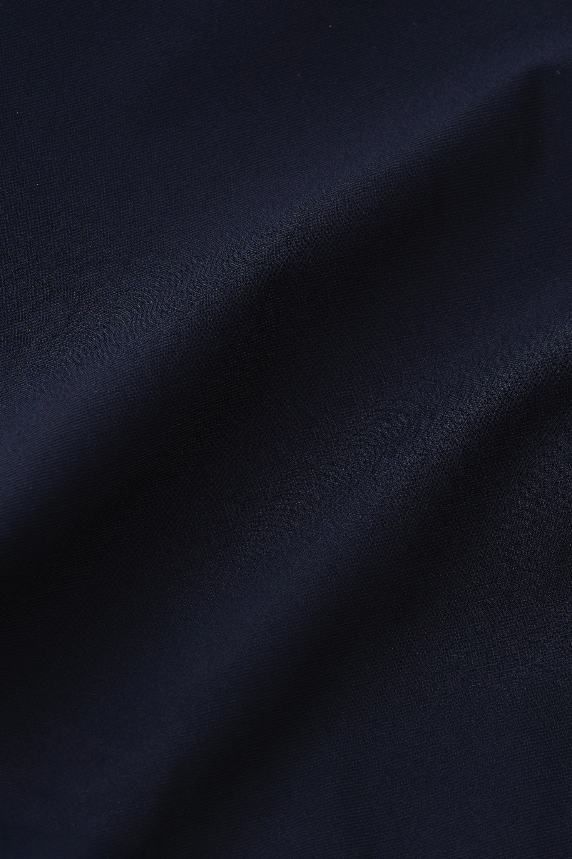 A close-up of Twillory's Event Polo Solid in Black shows wrinkle-free fabric, smoothly draped with gentle folds and a matte texture. Subtle highlights accent the contours, enhancing the sleek, sophisticated look.