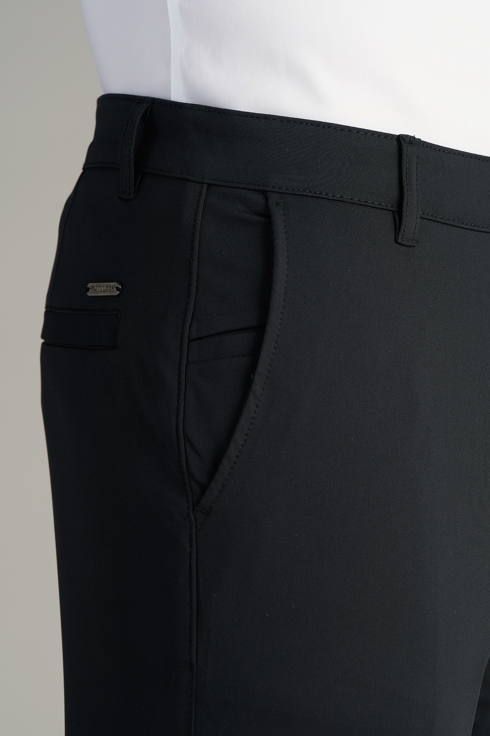 A close-up of someone in Performance Pants // BLACK, featuring side pockets and belt loops, paired with a tucked-in white shirt.