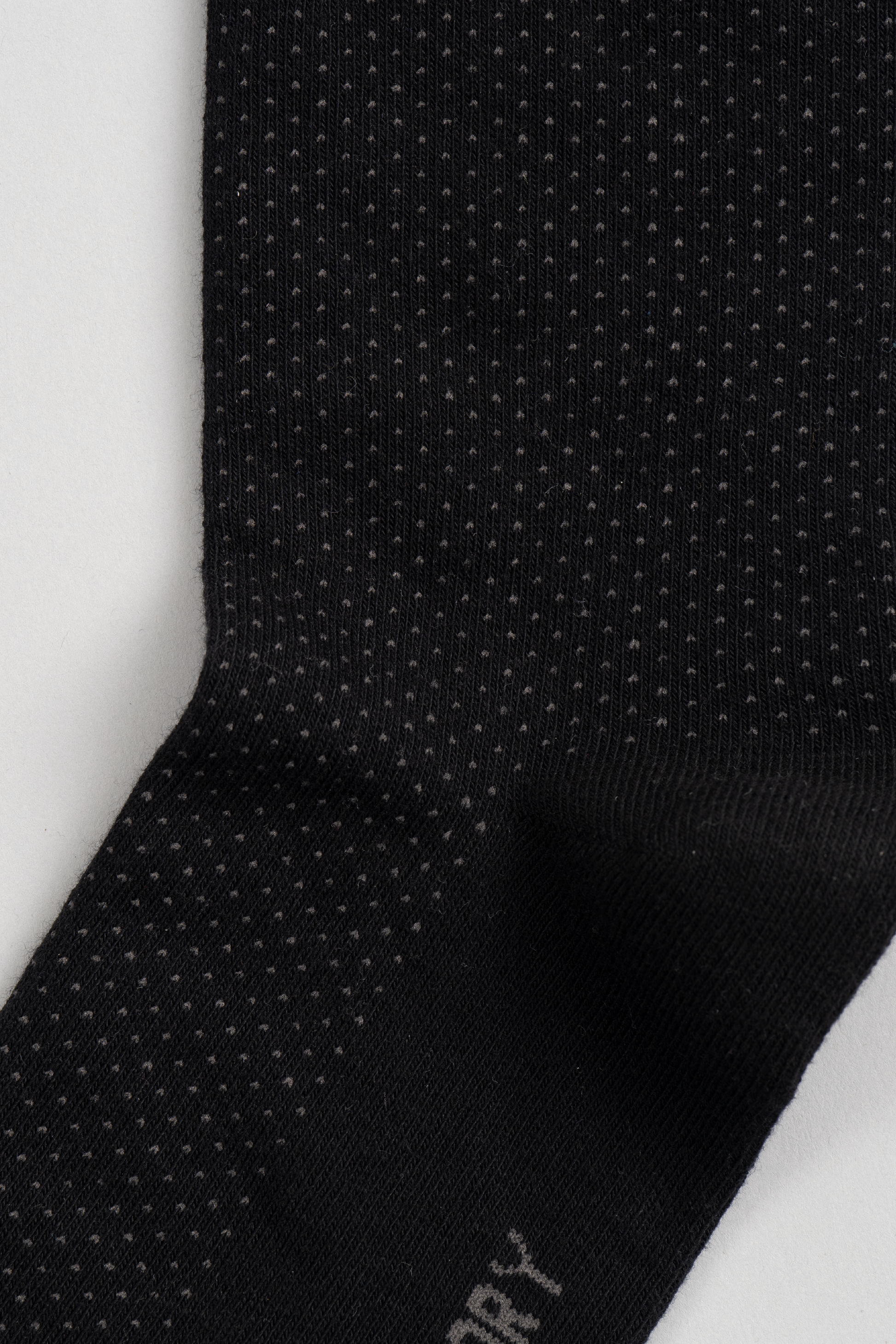 Close-up of Twillory's Black Pin Dot sock, showcasing small, evenly spaced white dots in vertical rows. The soft, stretchy material stands out against a plain light background, promising comfort and style.