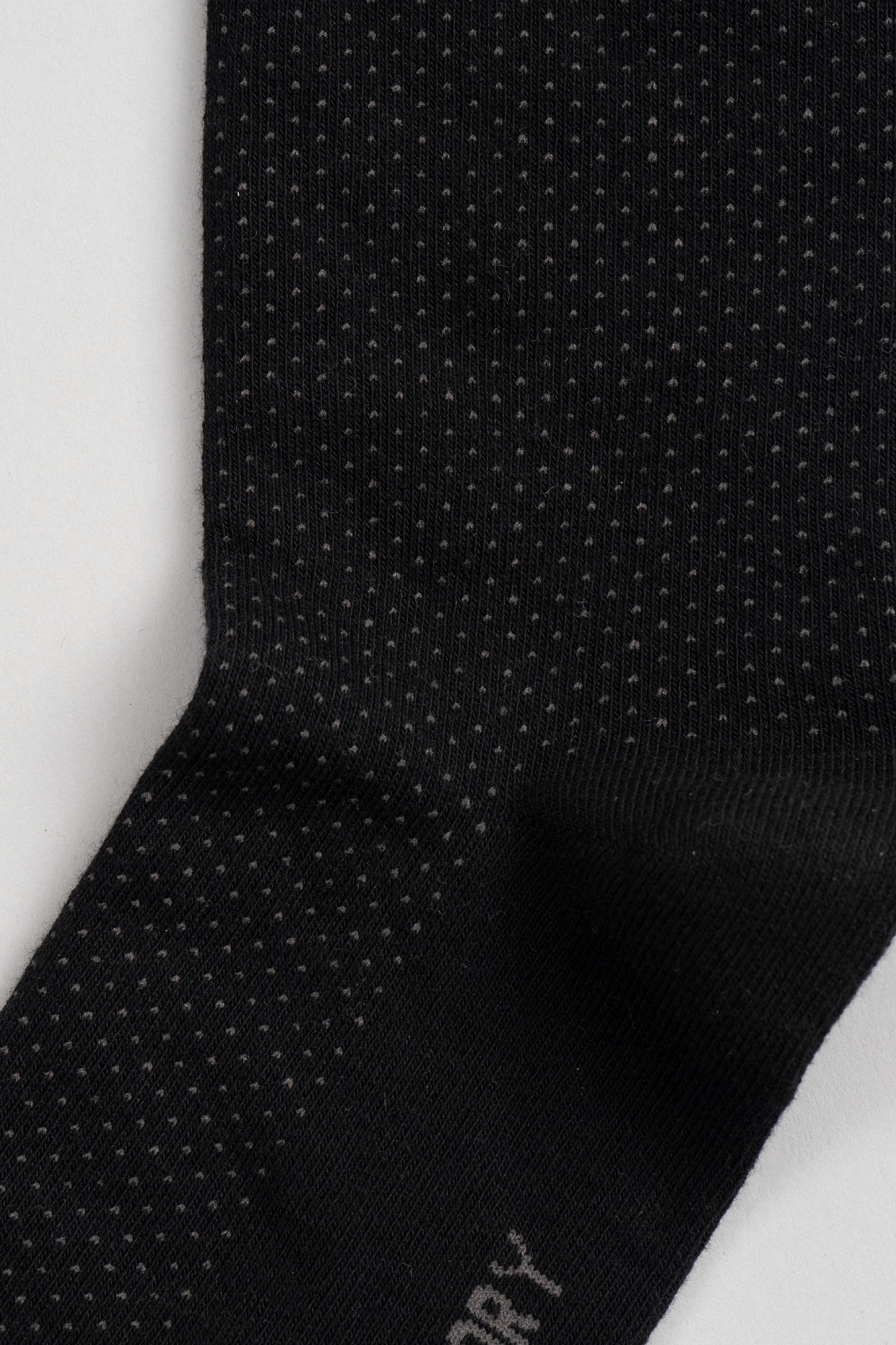 Close-up of Twillory's Black Pin Dot sock, showcasing small, evenly spaced white dots in vertical rows. The soft, stretchy material stands out against a plain light background, promising comfort and style.