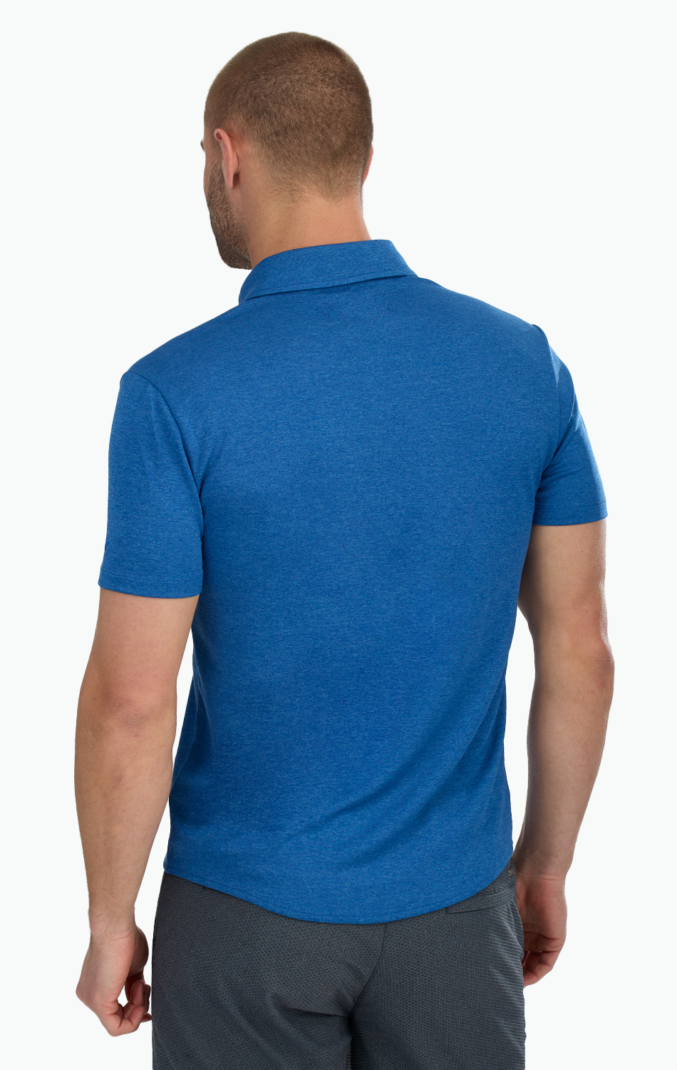 A man with short hair, seen from the back, wears a Twillory Short Sleeve Button Down Polo Solid in blue and dark gray pants. He stands against a white background, with his left arm slightly bent and right arm relaxed.