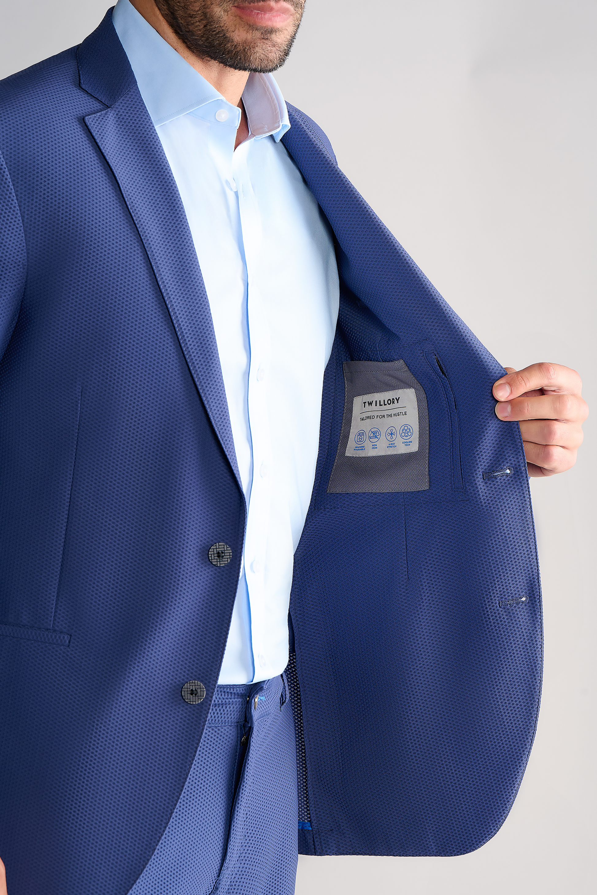 A man in the Twillory AIR Blazer // Blue, crafted from 360° airflow fabric, holds open his jacket to show the inner lining and chest pocket label; his face is partially out of frame to highlight the suit's details.