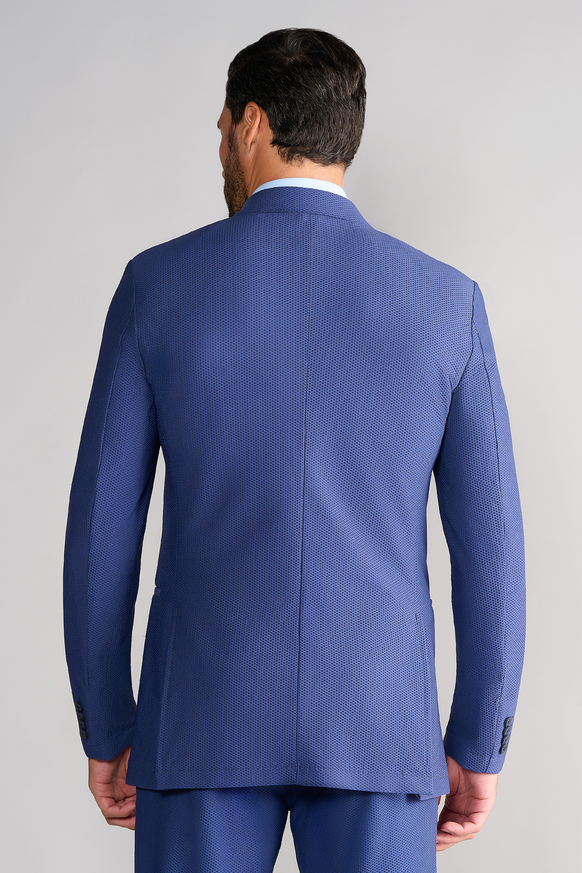 A man stands with his back to the camera, displaying the AIR Blazer // Blue by Twillory, crafted from 360° airflow fabric. His dark hair is neatly styled and arms relaxed at his sides, set against a plain light background.