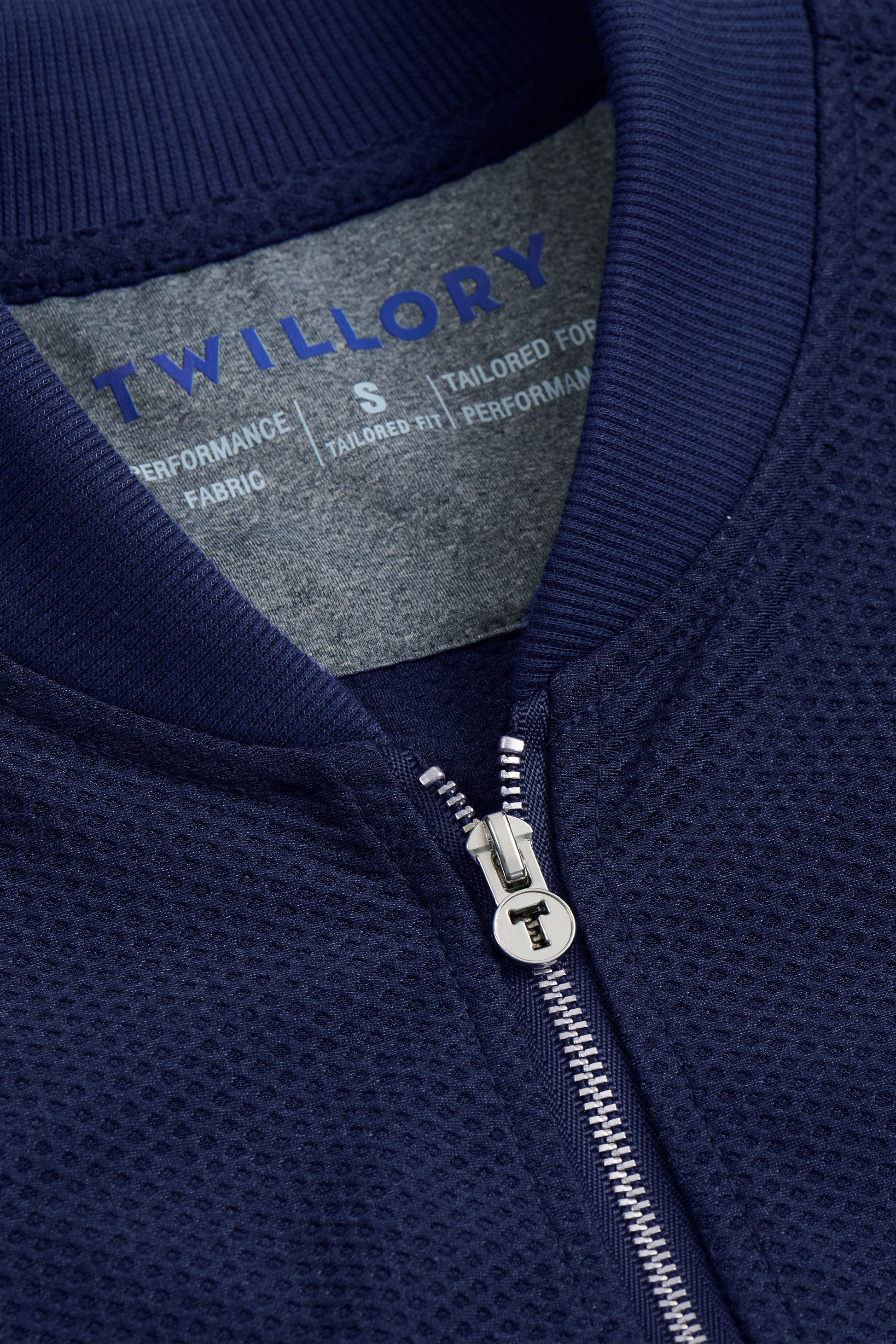 Close-up of the Twillory AIR Bomber // Blue, featuring a textured, breathable outer layer and metallic zip pull with "T." The inner label displays Twillory branding, size S, and fabric info in white text.