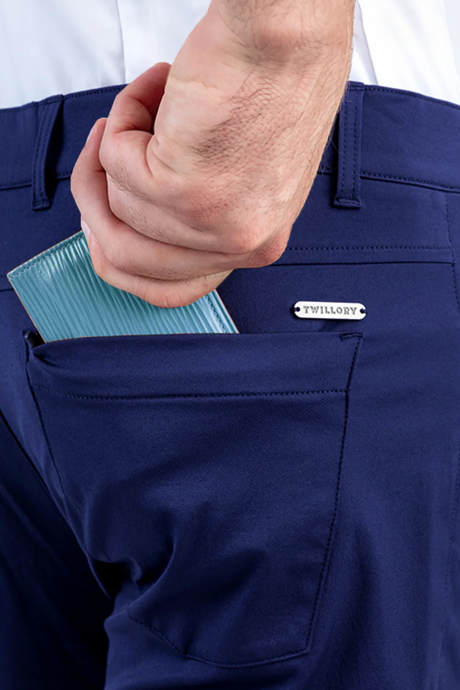 A close-up shows a person sliding a light blue wallet into the back pocket of Twillory's Performance Five Pocket // BLUE pants, featuring a small metal “Twillory” label. They’re also wearing a tucked-in white 4-way stretch shirt.