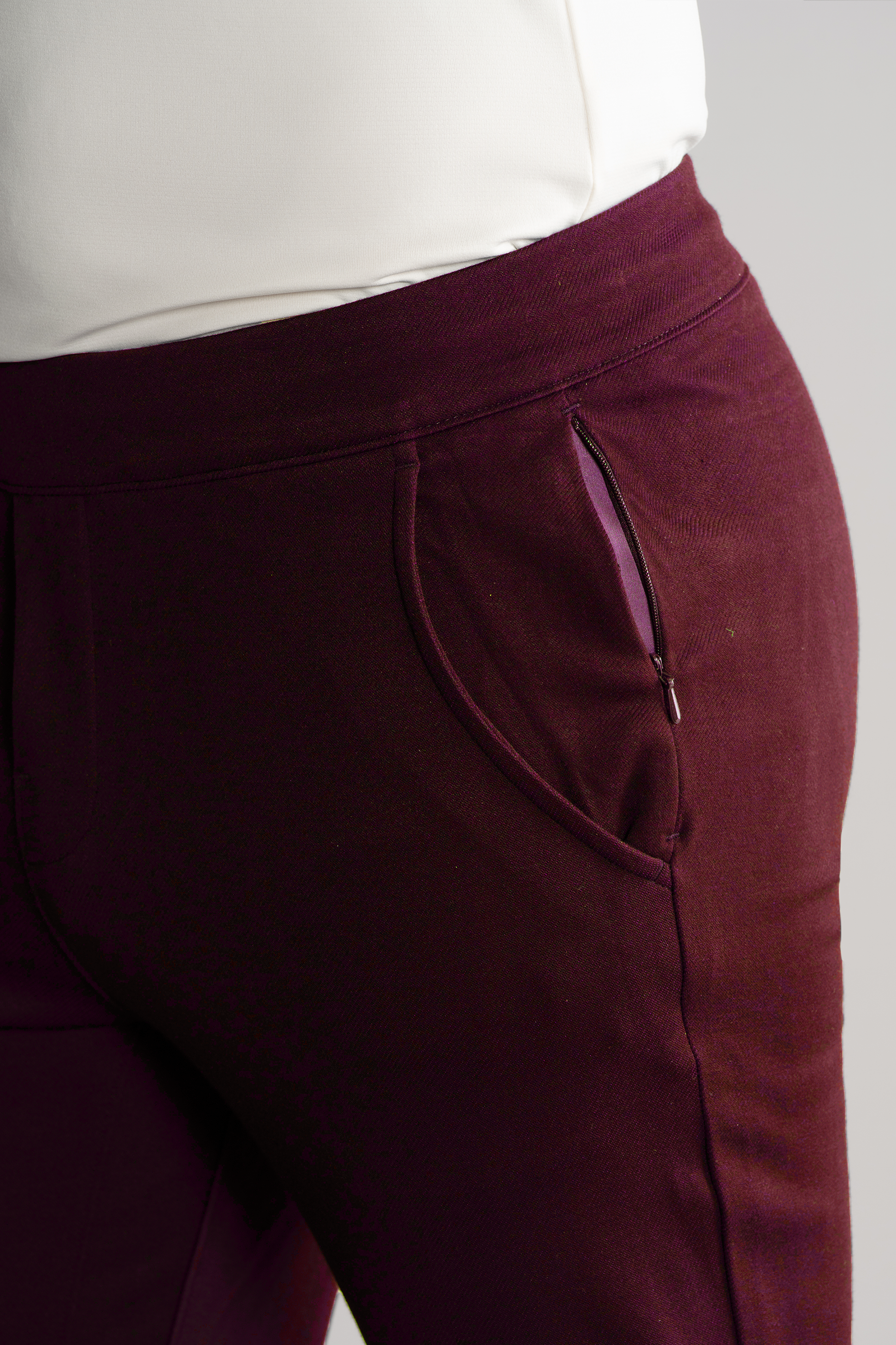 A close-up shows the Twillory Athlounger Jogger in burgundy, featuring a side-zip pocket. The white top is tucked in to highlight the smooth comfort fabric and the waist and upper thigh area.