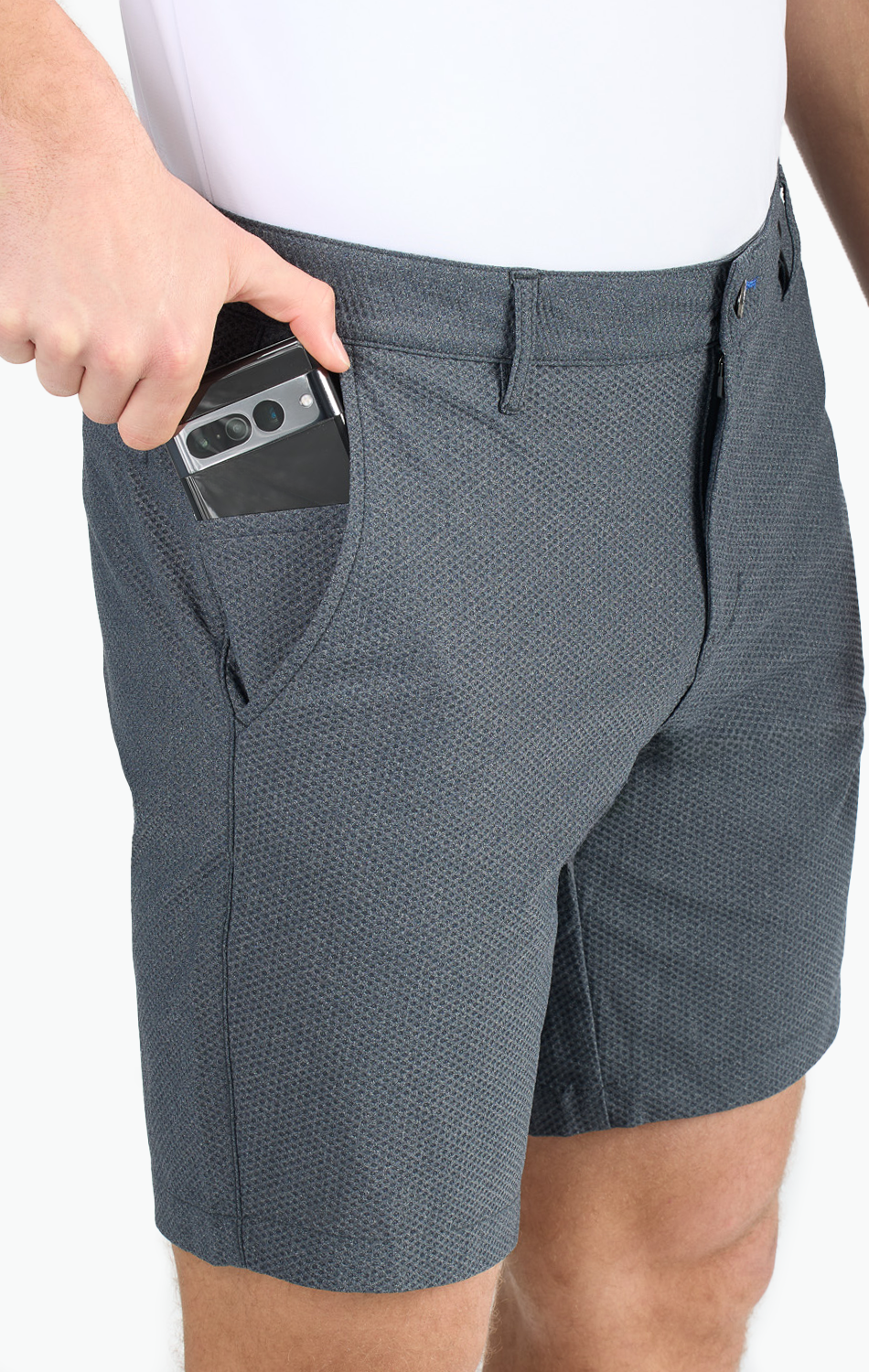 Man wearing dark gray textured shorts, slipping a smartphone into the side pocket, demonstrating pocket size and convenience.