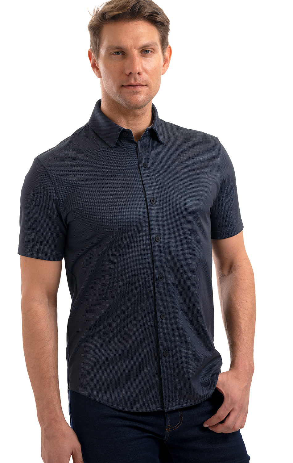 A man with short light brown hair wears a Twillory Short Sleeve Button Down Polo Dot in Charcoal and dark jeans. He stands facing forward against a white background, left hand in his pocket, right arm relaxed by his side.