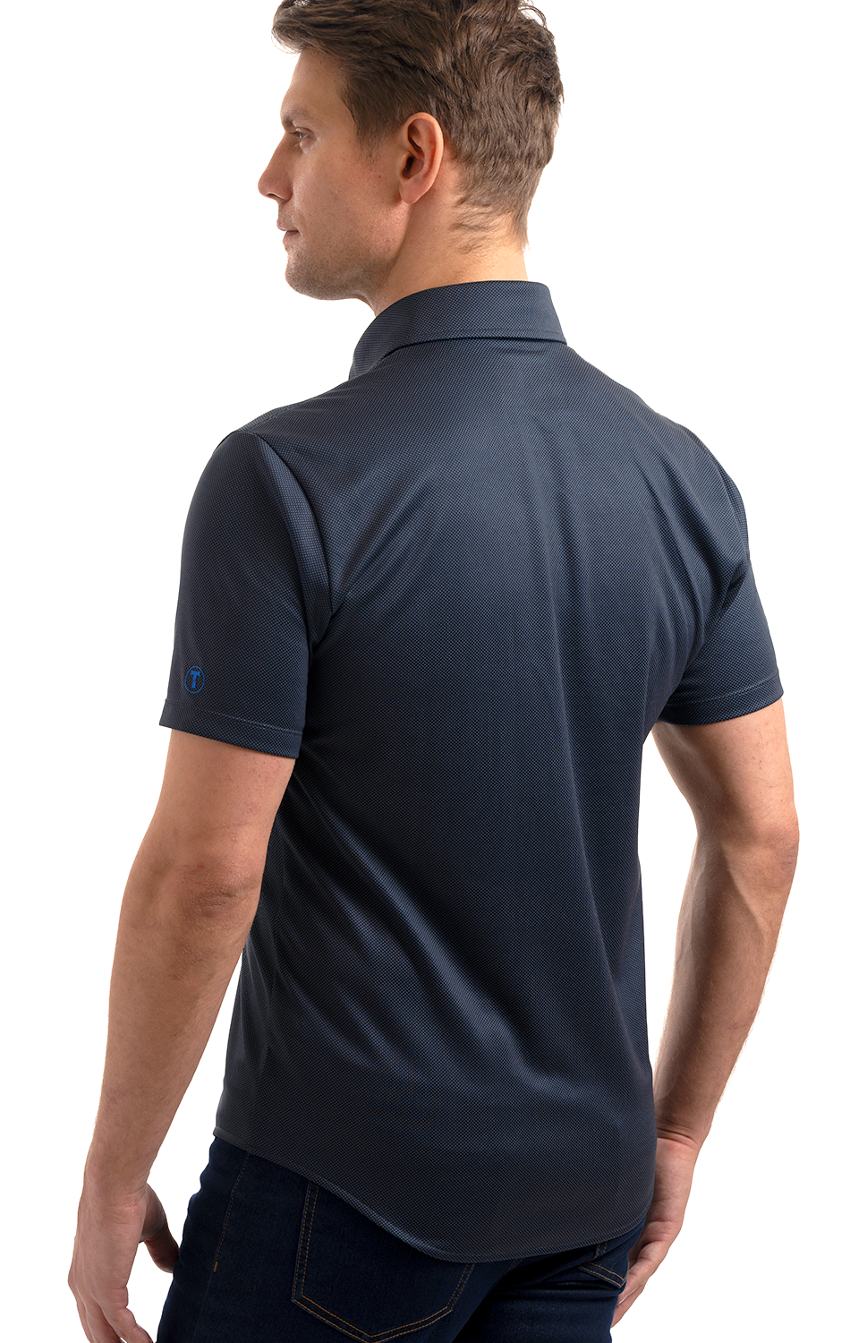 A man stands turned slightly to the side, wearing the Twillory Short Sleeve Button Down Polo Dot in charcoal and dark jeans. The wrinkle-free shirt features a subtle sleeve logo. A white background highlights his outfit.