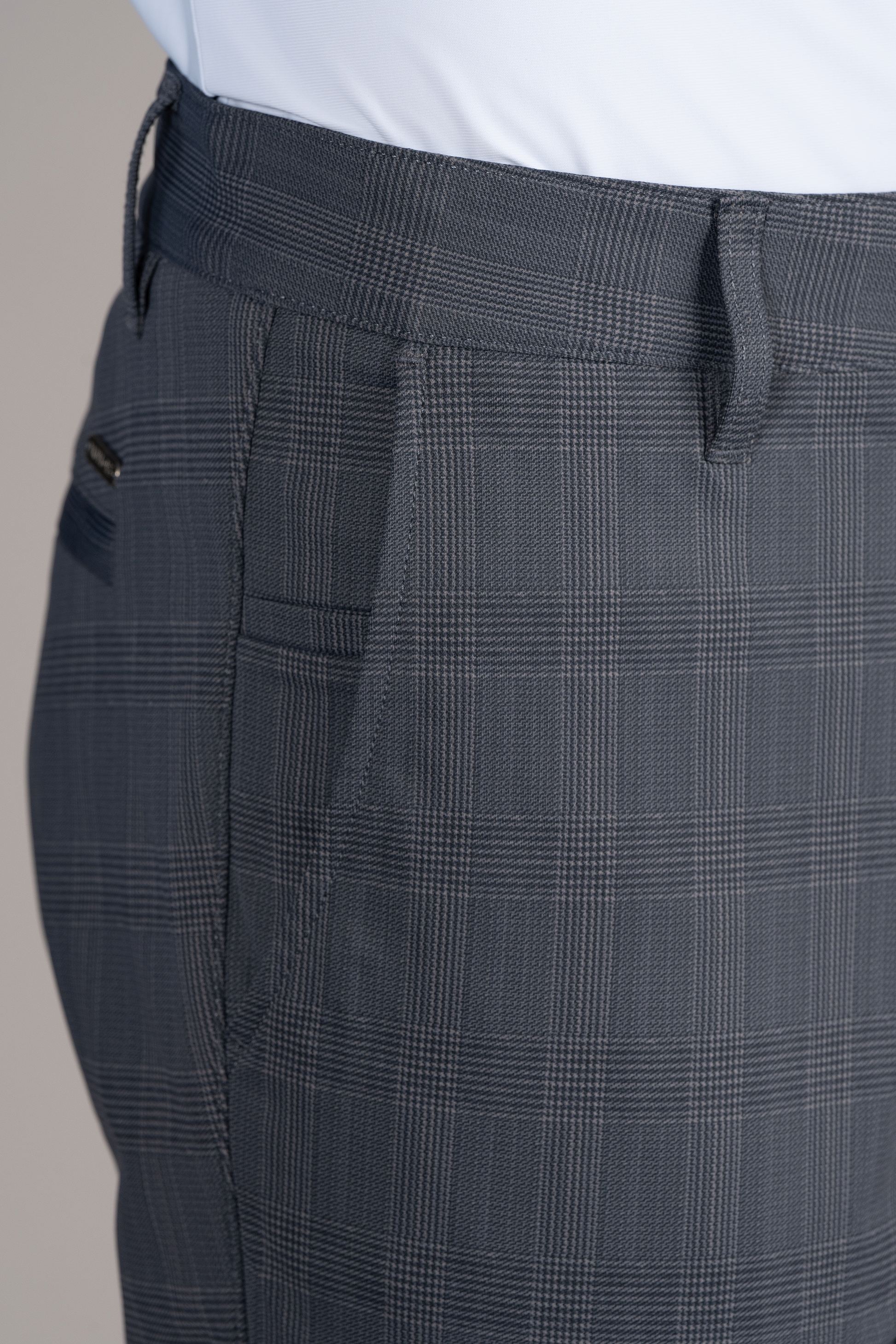 Close-up of a person wearing Twillory's Performance Pants // Grey Prince of Wales, featuring stretch fabric, belt loops, side pocket, and welted back pocket. A white shirt is tucked into the waistband above the subtle check pattern.