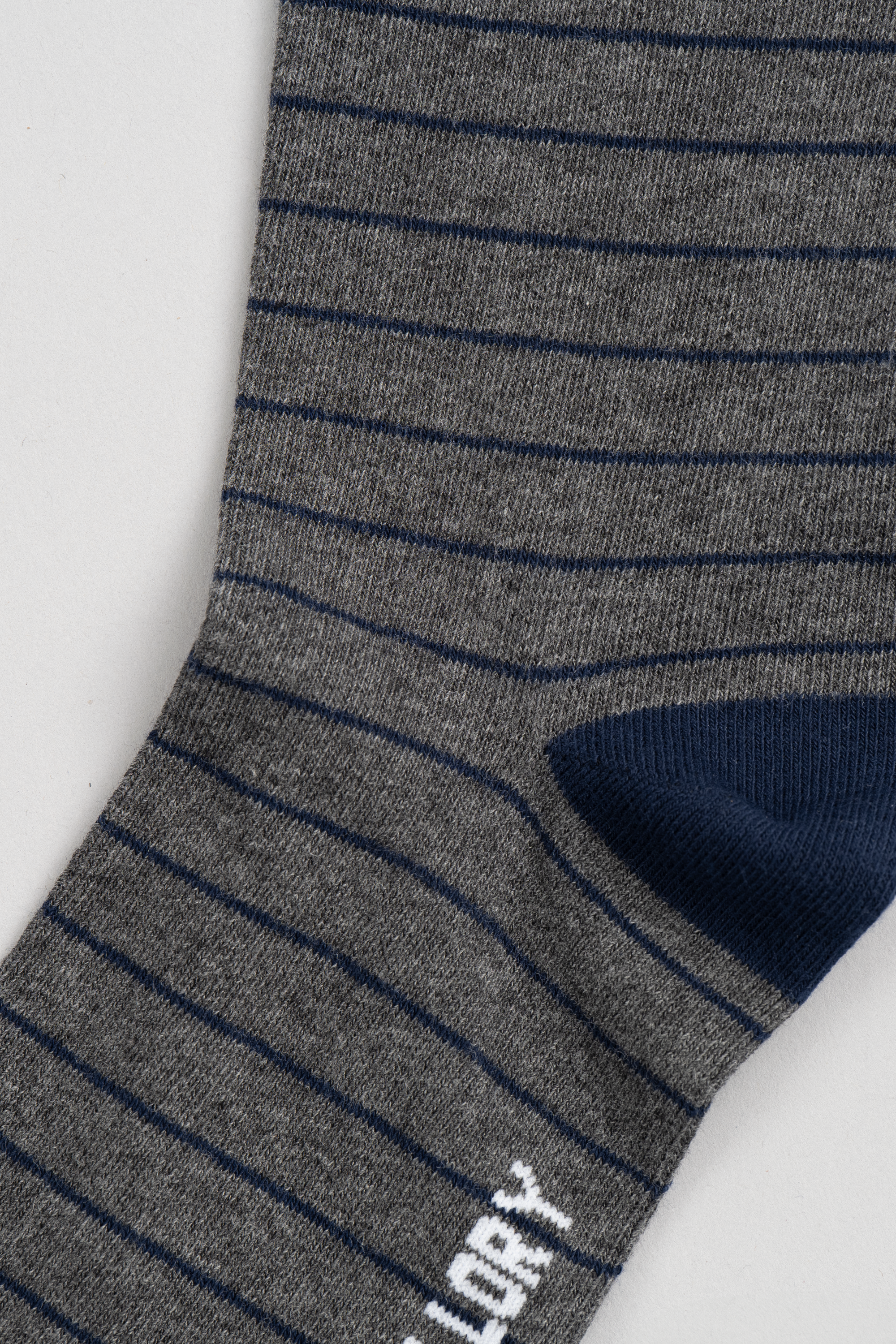 A close-up of Twillory’s Grey Stripe sock featuring thin navy stripes on gray, a solid navy heel, and a partial white logo—perfect for upgrading your favorite sock collection.