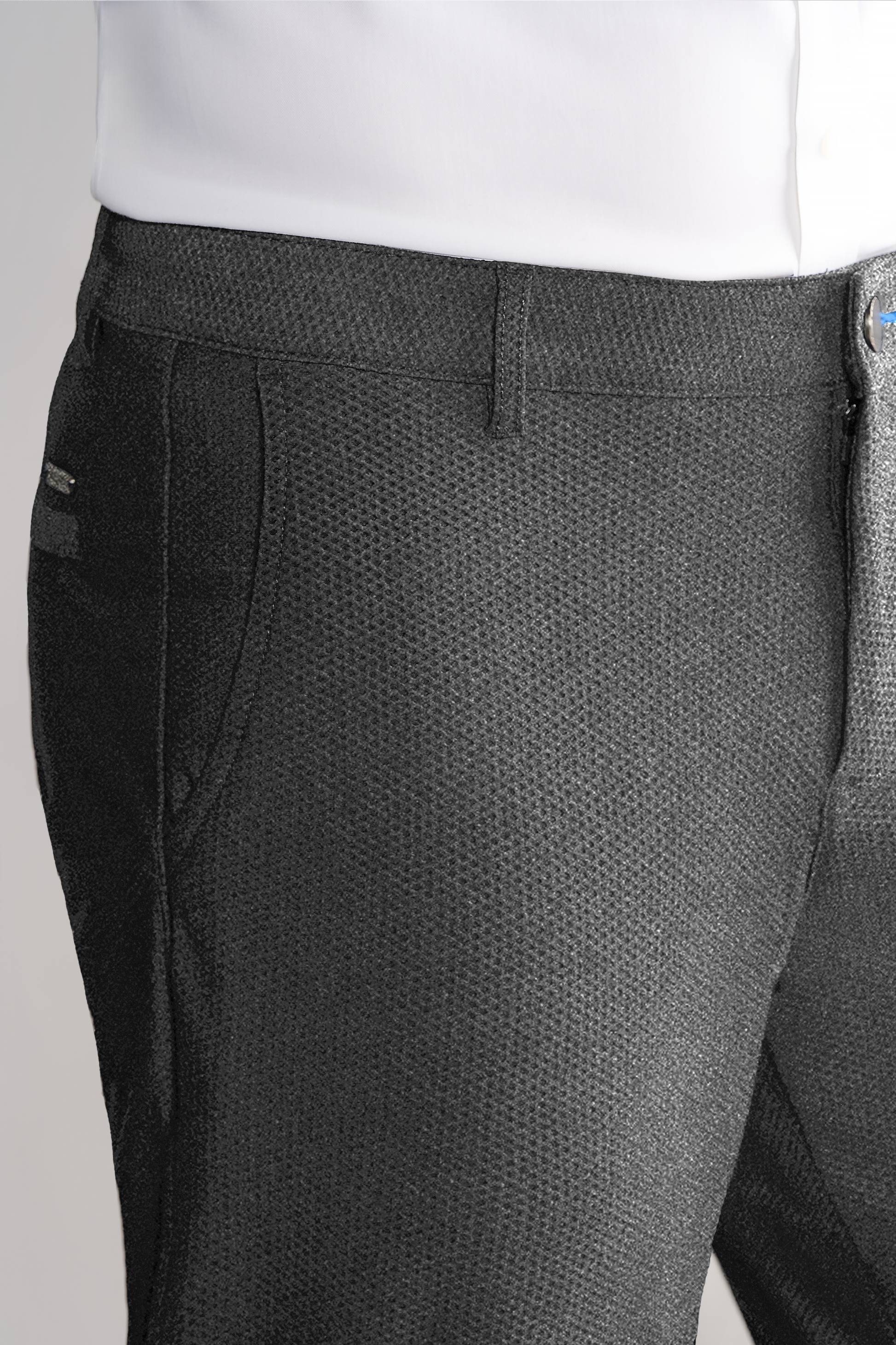 A close-up of a person wearing Twillory AIR Pants in Heather Grey, featuring 4-way stretch, side pockets, a subtle patterned weave, and visible waistband, belt loop, and zipper details. The white top is tucked in.