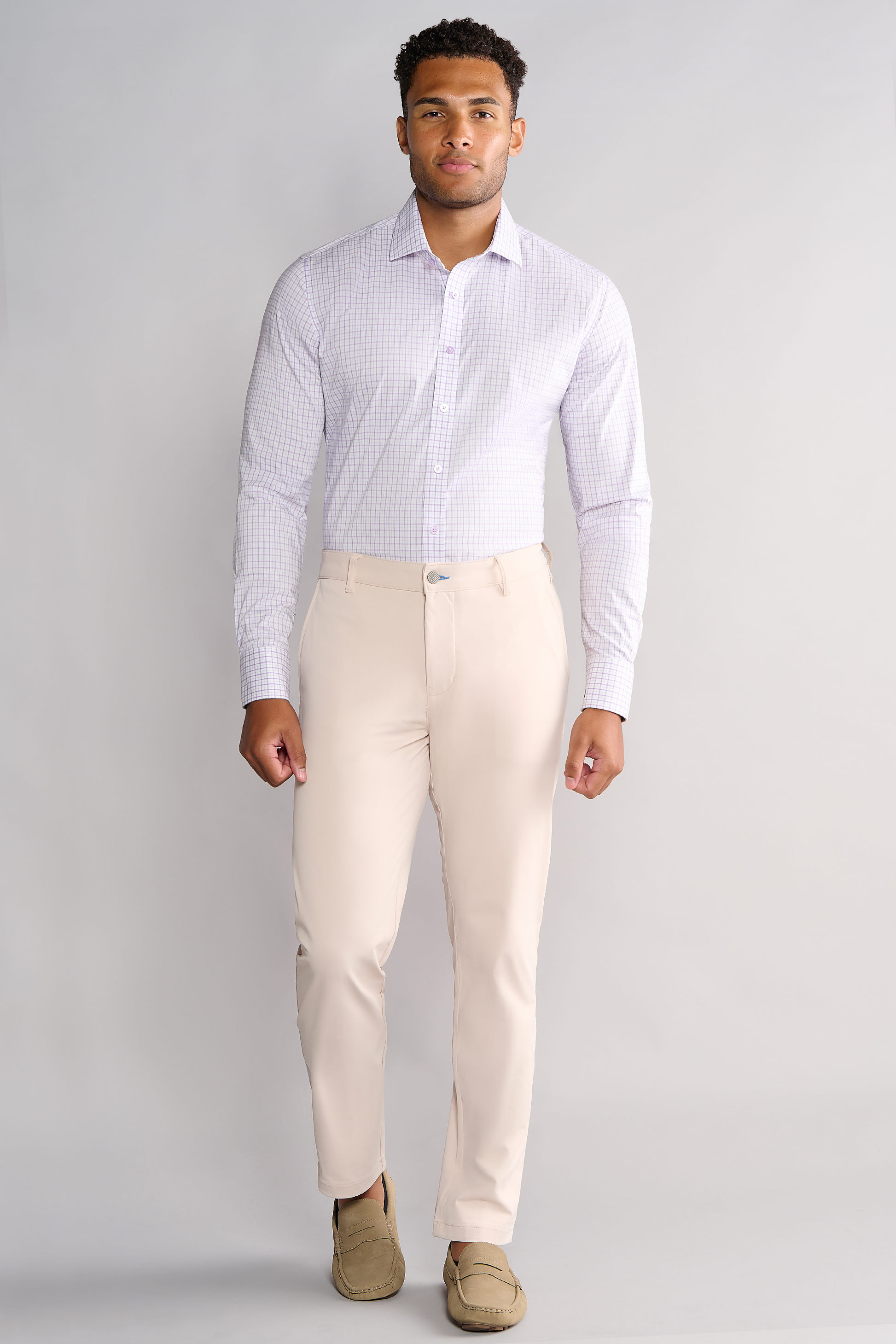 A man stands facing forward against a plain light background, wearing the Twillory Leader Windowpane // Lavender performance shirt with moisture-wicking fabric, tucked into beige dress pants and tan loafers. Sleeves are buttoned; arms relaxed at his sides.