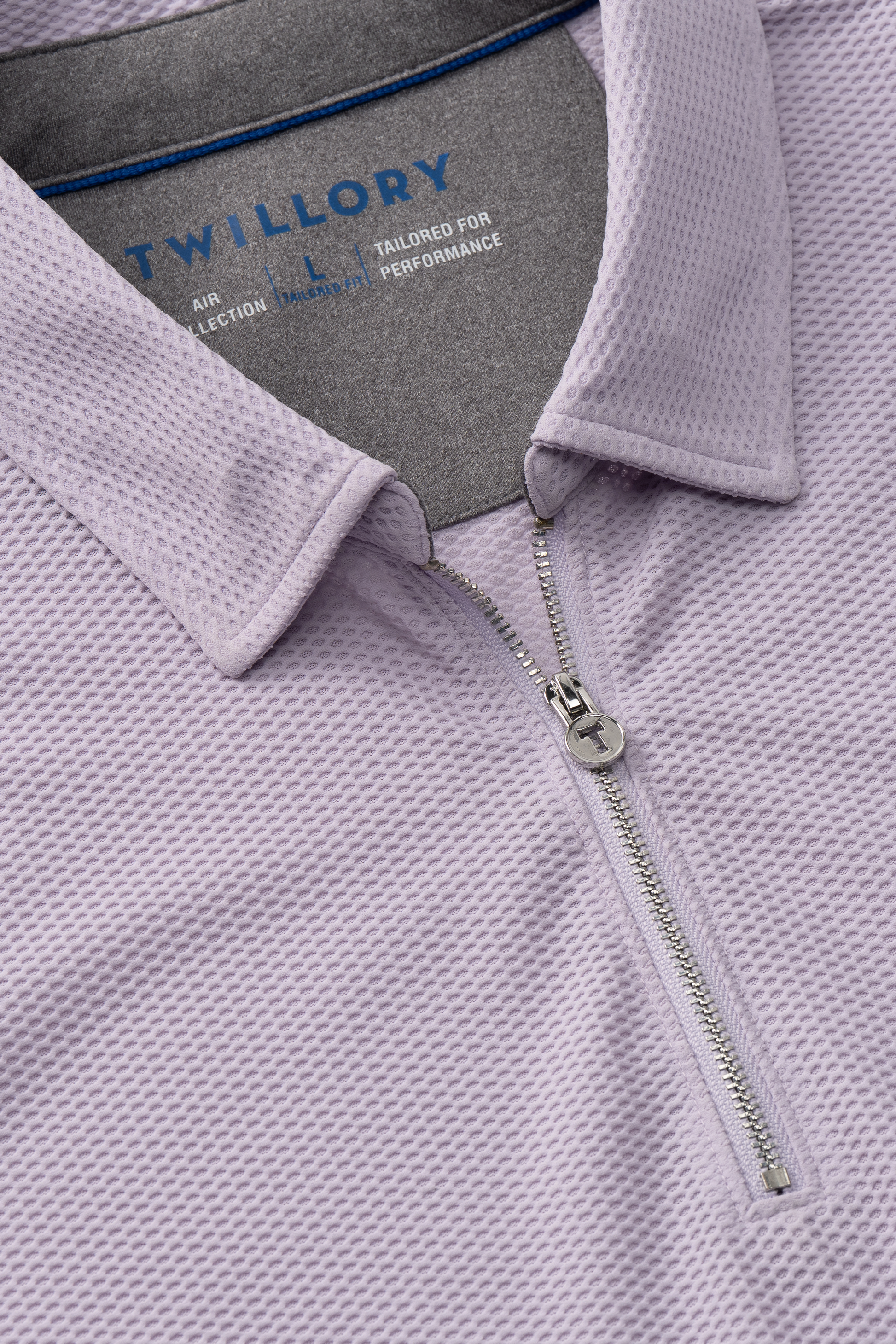 Close-up of the Twillory AIR Zip Polo Solid in Lilac—a light purple, hyper-breathable quarter-zip with a silver zipper. Features a folded collar revealing a blue and white neck label and 360° Airflow waffle-knit fabric for comfort.