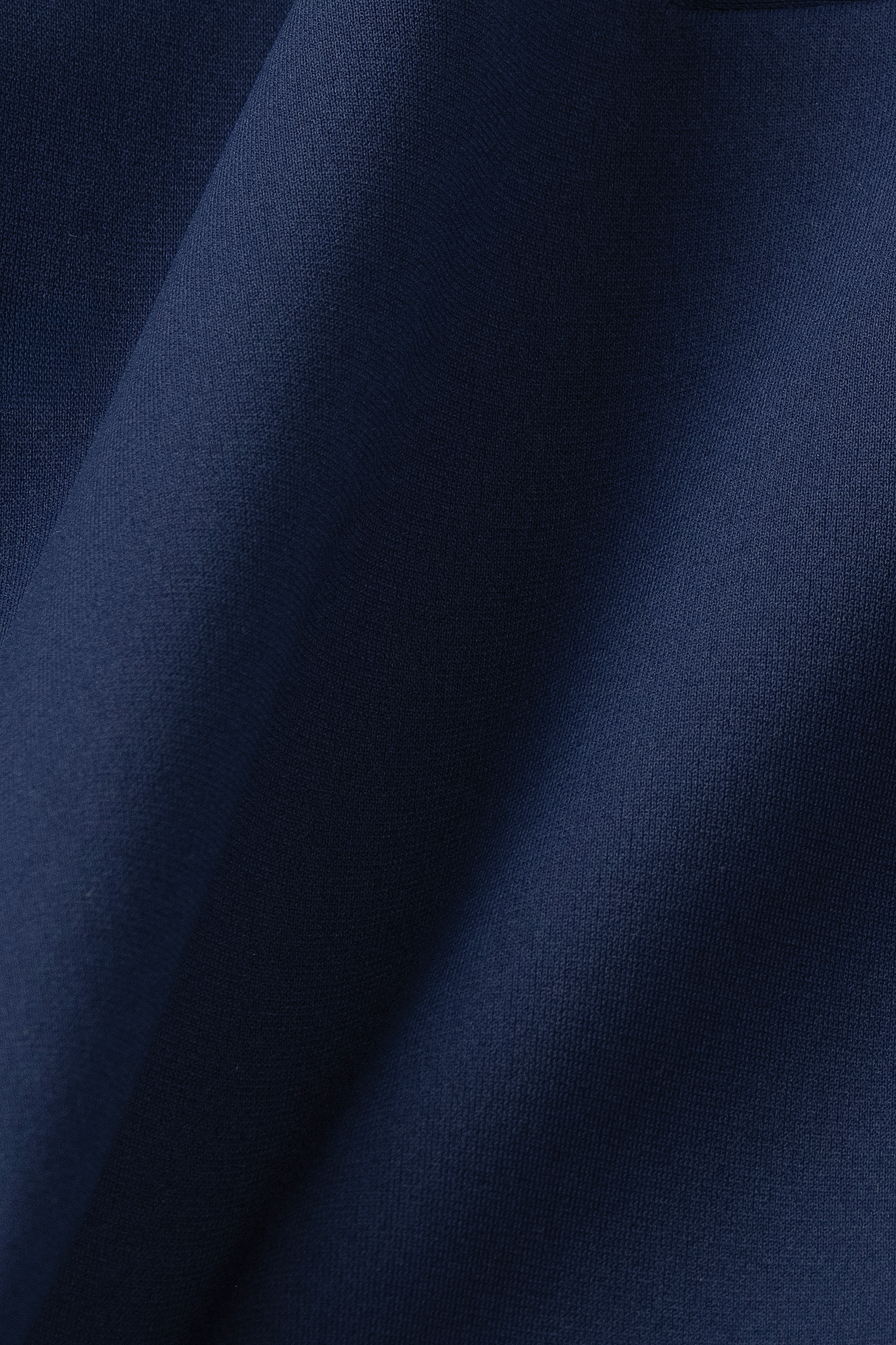 A close-up of the Twillory Performance Blazer // Navy shows smooth, dark navy fabric with soft folds and shadows, emphasizing its texture and drape. Lighting reveals subtle variations in blue across the surface.