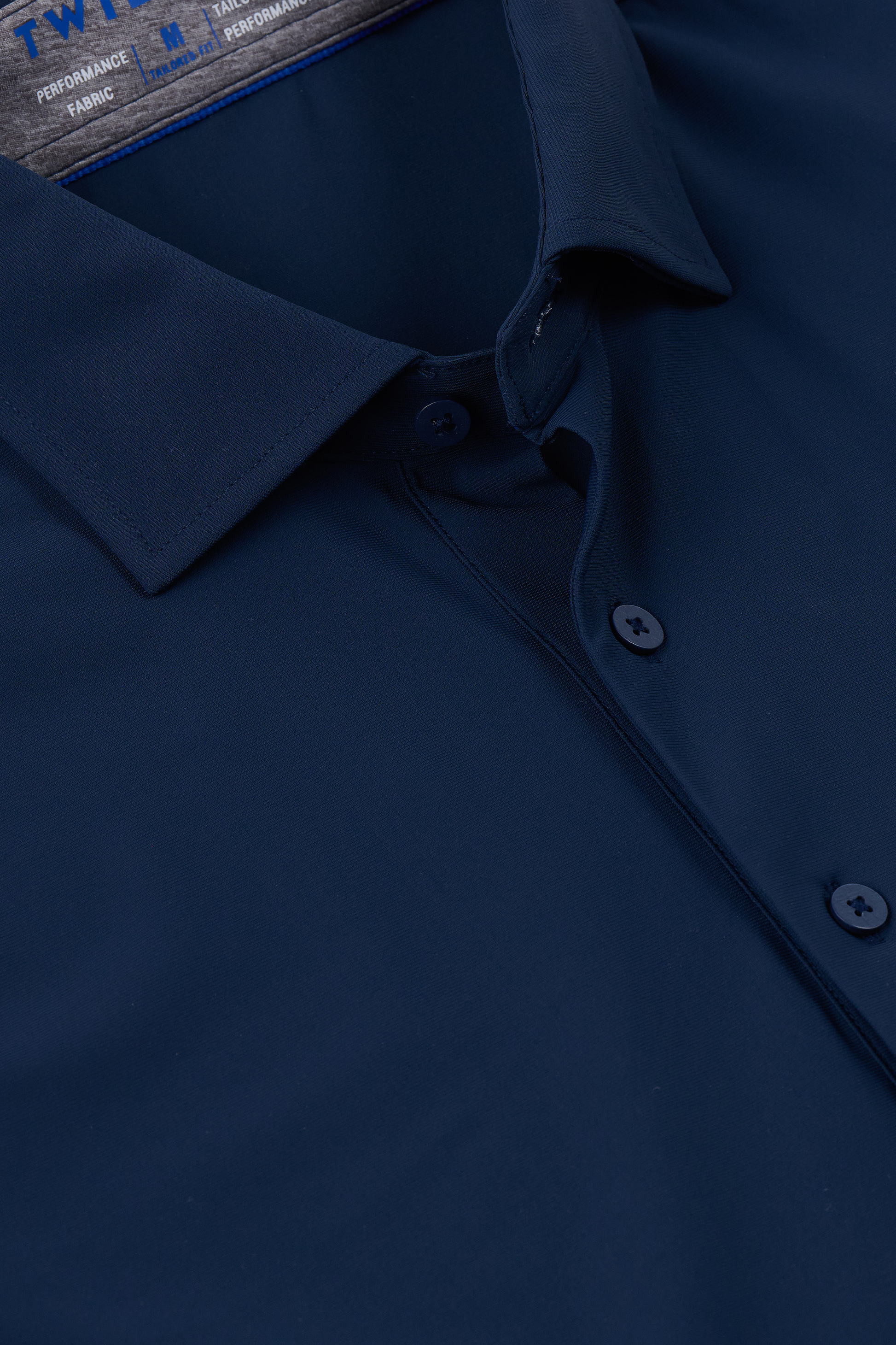 Close-up of the Twillory Event Polo Solid in Navy. The smooth, slightly shiny fabric is wrinkle-free with performance stretch. Features a pointed collar, two blue buttons on the placket, and a label inside the collar with blue and white text.