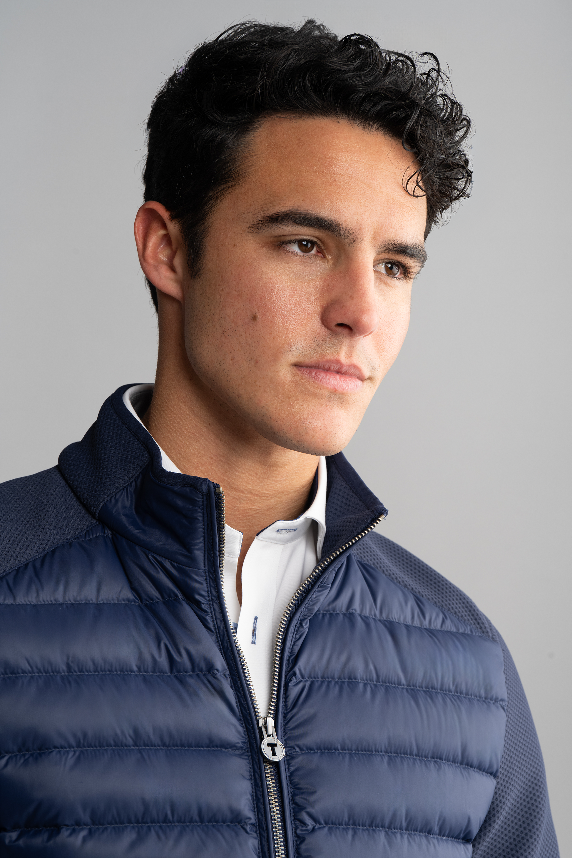 A young man with short, wavy dark hair wears the Twillory Central Hybrid Jacket in Navy over a white collared shirt. He looks slightly to the side with a neutral expression against a plain light gray background.