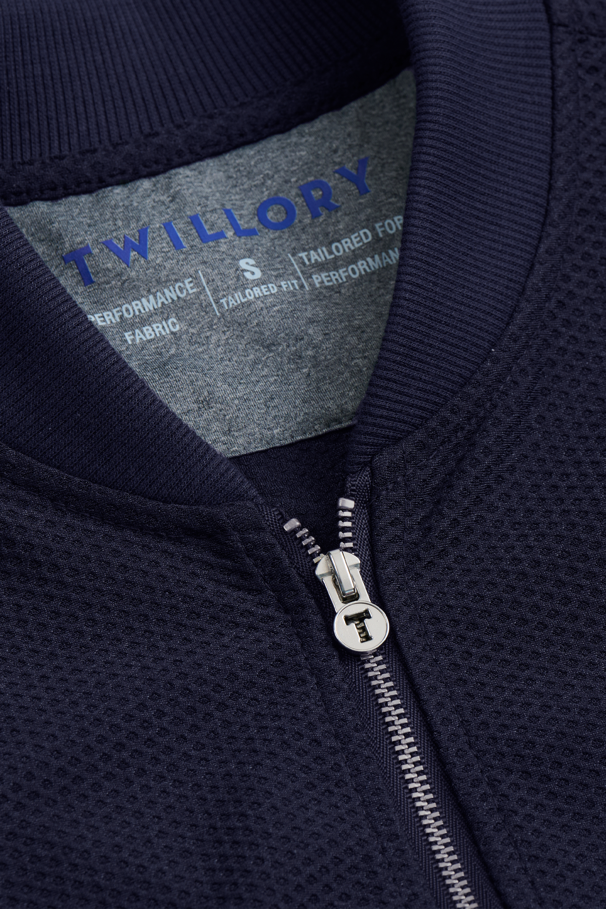 Close-up of the Twillory AIR Bomber // Navy’s textured collar and silver zipper. Inside, a gray label with blue “TWILLORY” text and size “S.” The honeycomb 360° Airflow Fabric ensures this jacket is a breathable outer layer.