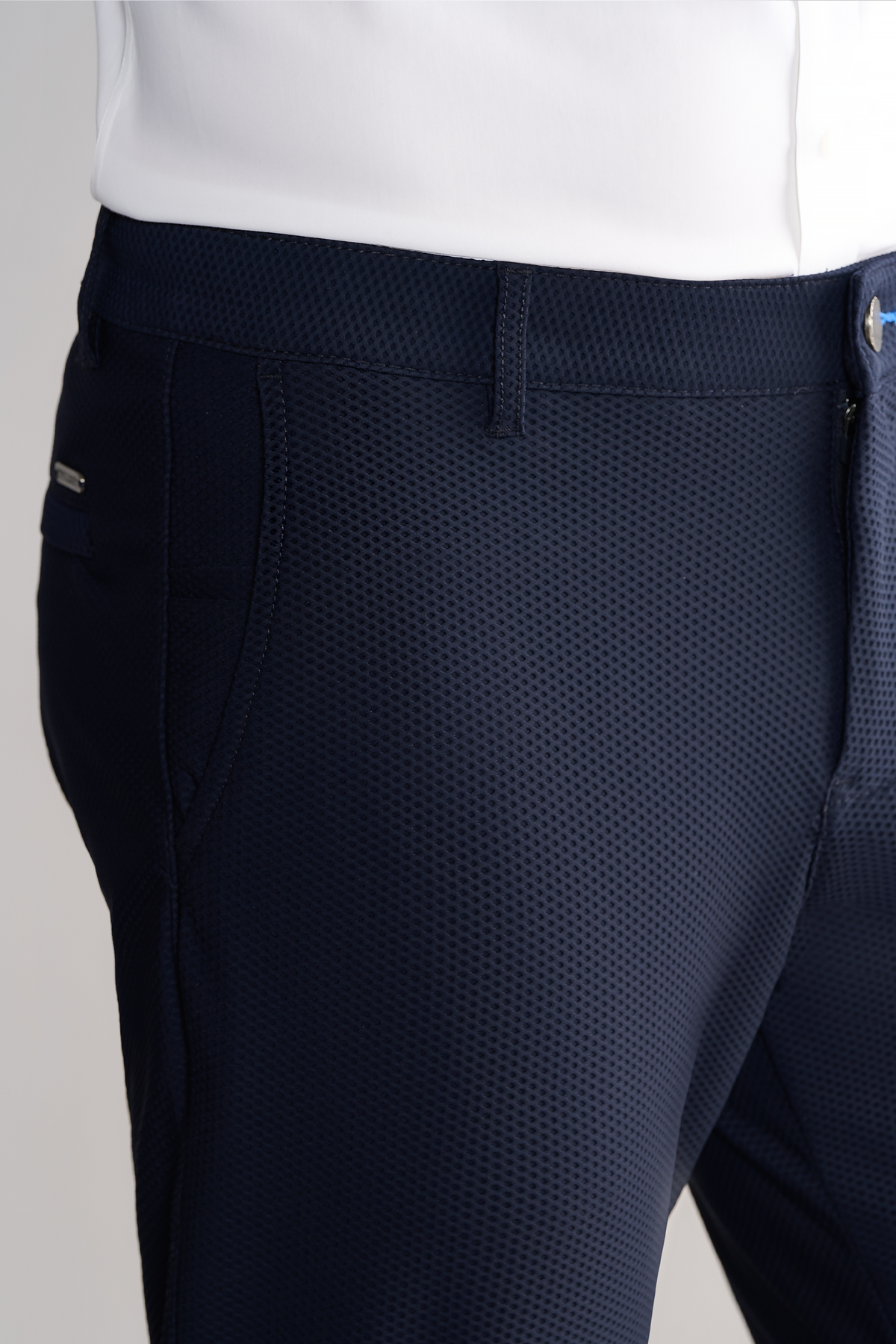 Close-up of a person wearing Twillory AIR Pants // Navy, featuring 4-way stretch performance fabric with a fine waffle-like texture, front pockets, and belt loops—paired with a tucked-in white shirt for comfort and flexibility.