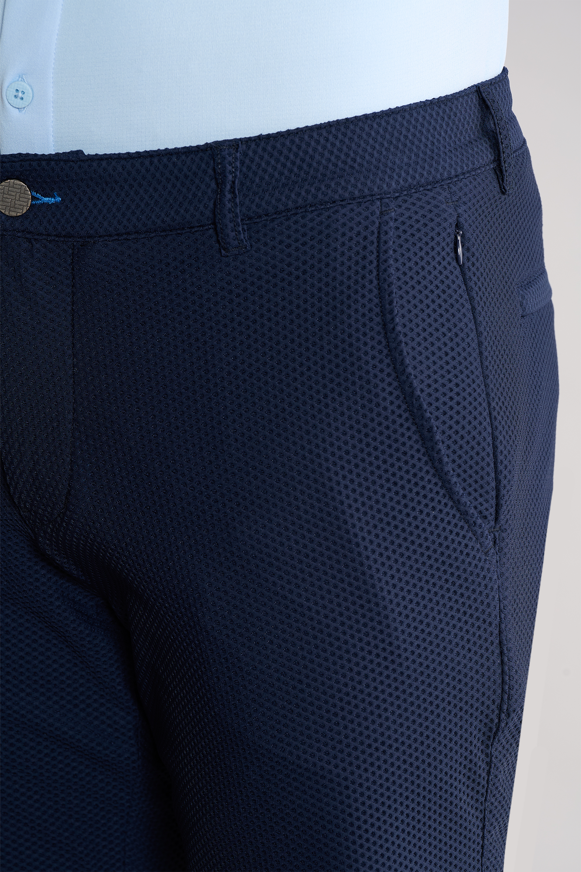 Close-up of a person wearing Twillory AIR Shorts in textured navy blue with a dot pattern, side pocket, waistband, belt loop, and zipper. These sweat-wicking shorts offer comfort. A light blue shirt is tucked in.