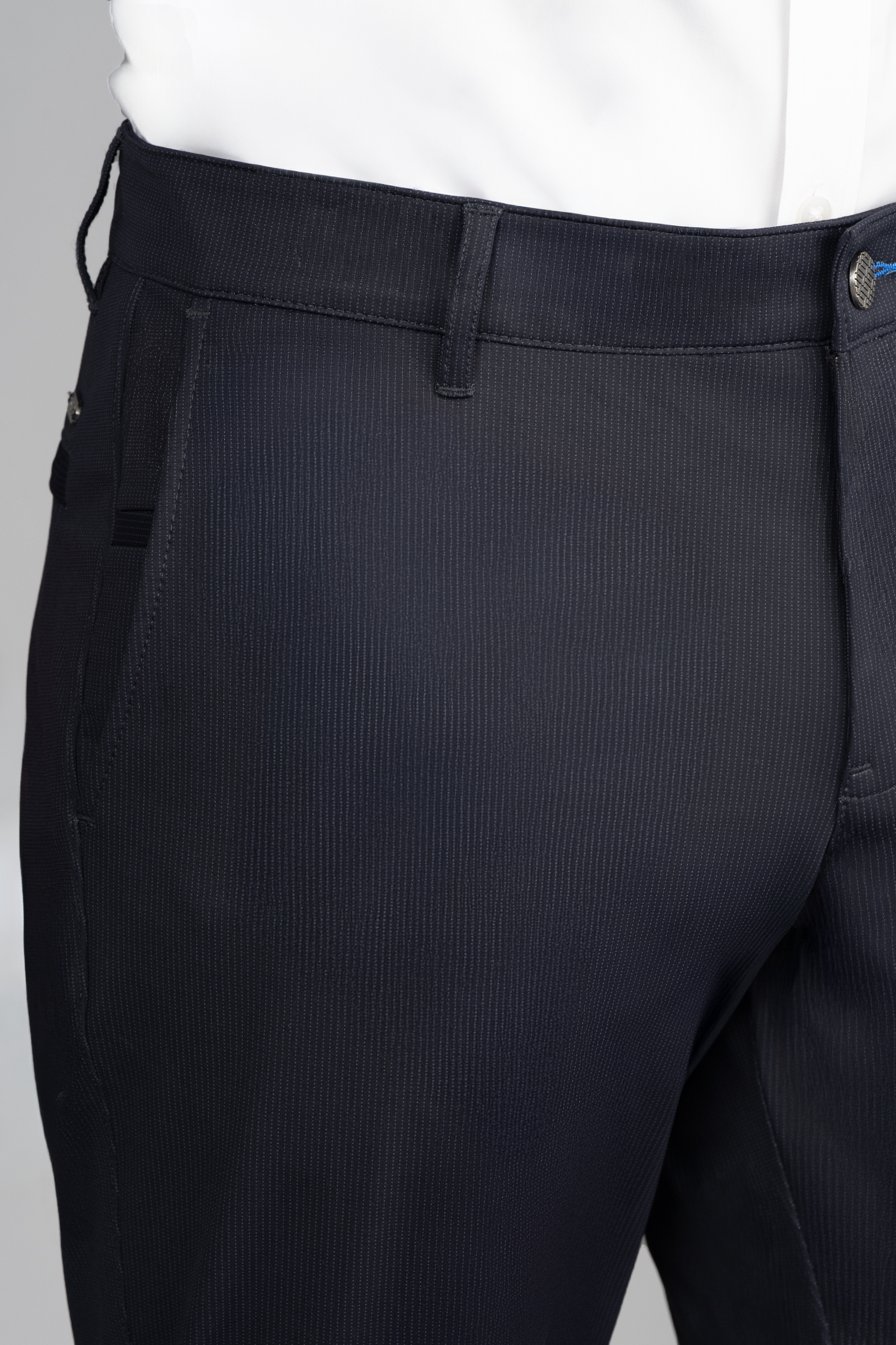 A close-up of a person in Twillory’s Performance Pants // Navy Pin Stripe, featuring 4-way stretch, subtle pinstripes, belt loops, side pockets, and a button closure with a white shirt tucked in against a neutral gray background.