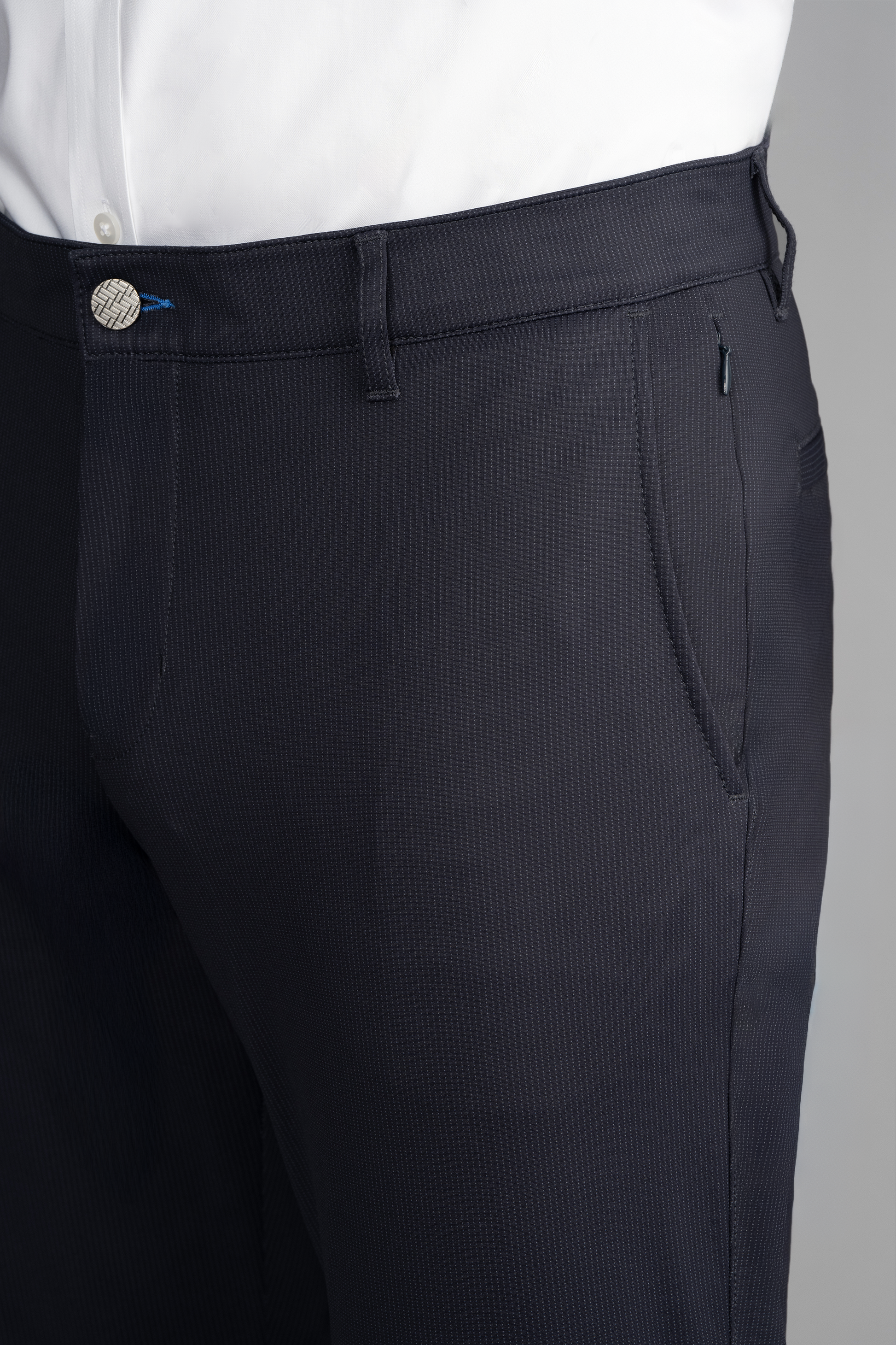 A close-up of a person wearing Twillory Performance Pants // Navy Pin Stripe featuring 4-way stretch, subtle vertical stripes, belt loops, a metallic button, blue thread accent near the waistband, and paired with a tucked-in white shirt.