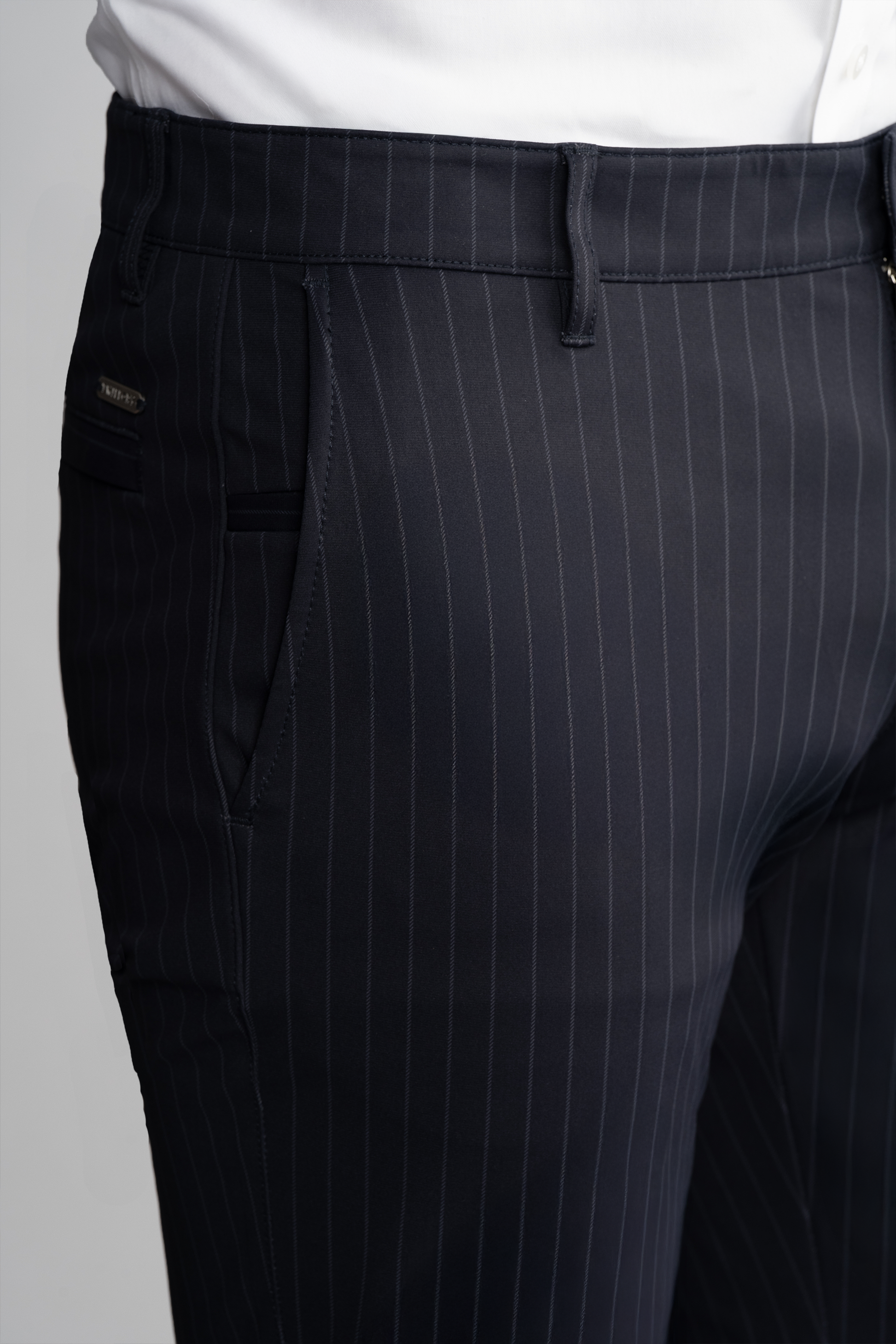 Close-up of a person wearing Twillory Performance Pants // Navy Stripe, featuring vertical white pinstripes, belt loops, side pocket, and paired with a tucked-in white shirt. Only the waist and upper legs are visible.
