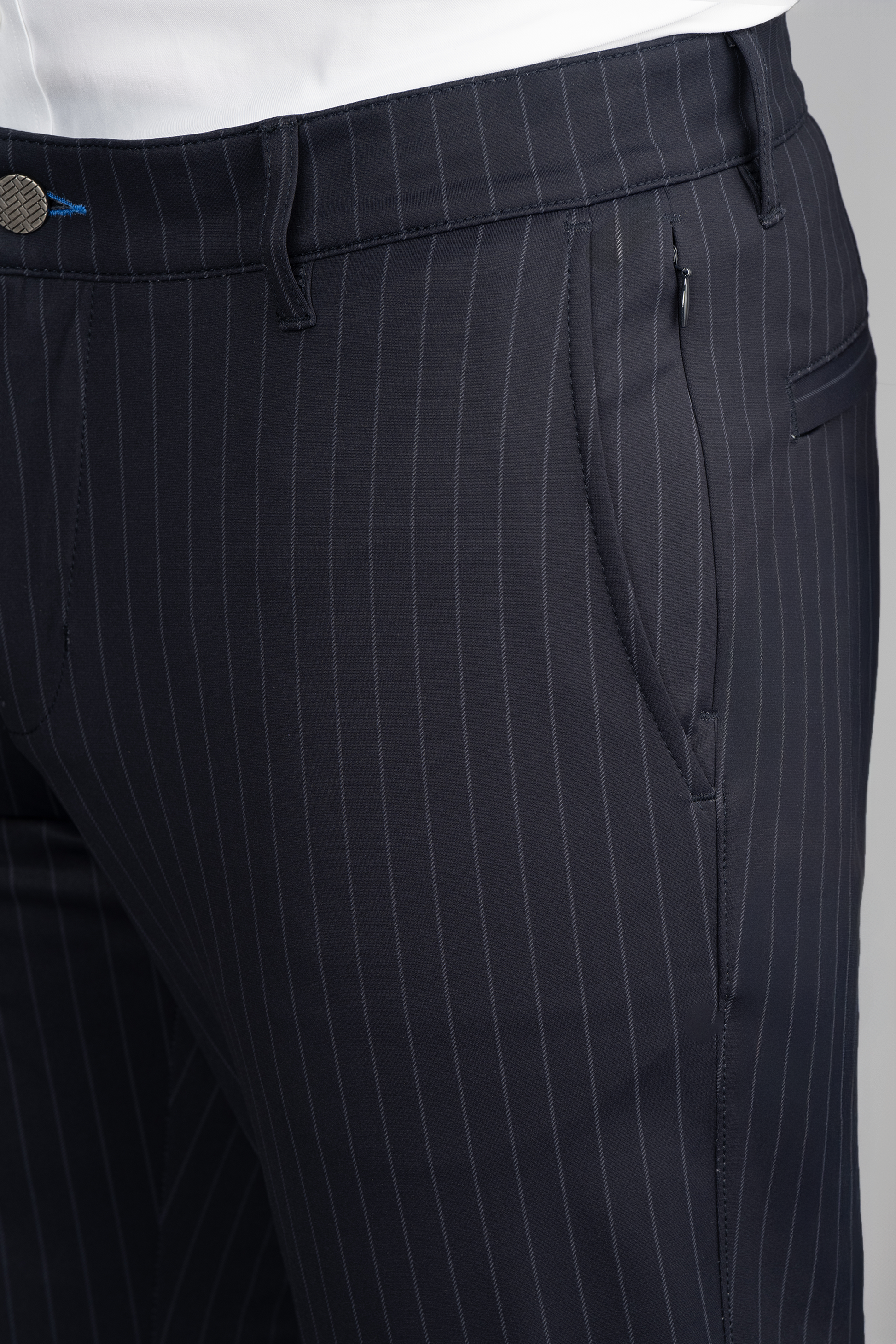 Close-up of a person wearing Twillory Performance Pants // Navy Stripe with a white shirt tucked in. The pants feature thin vertical stripes, front pockets, belt loops, a visible waistband button, and smooth, tailored performance fabric.