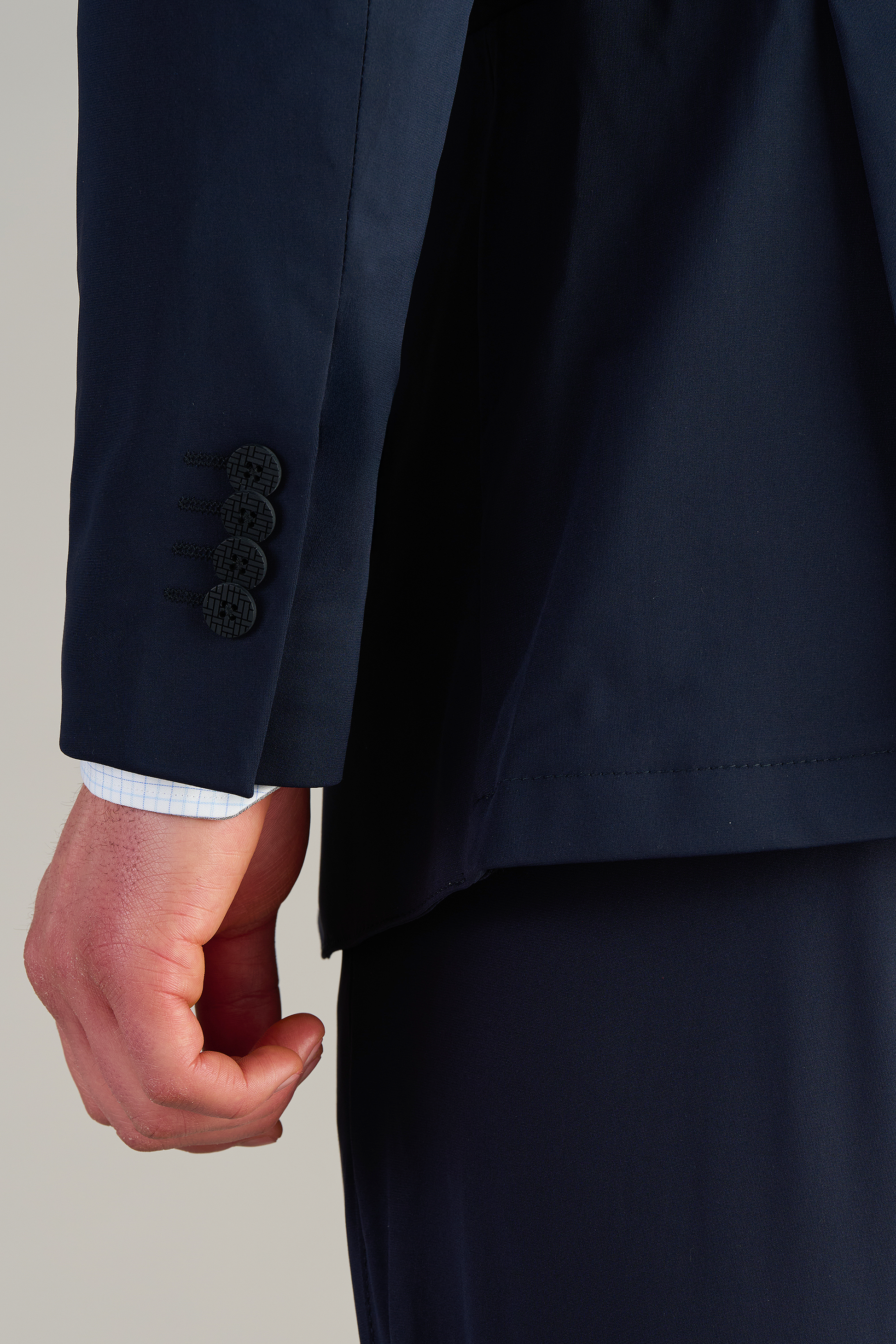 A close-up of a person’s left arm in Twillory’s Performance Blazer // Navy Blue, featuring four dark buttons and a white cuffed shirt. The plain background highlights the formal, stretch fabric design.