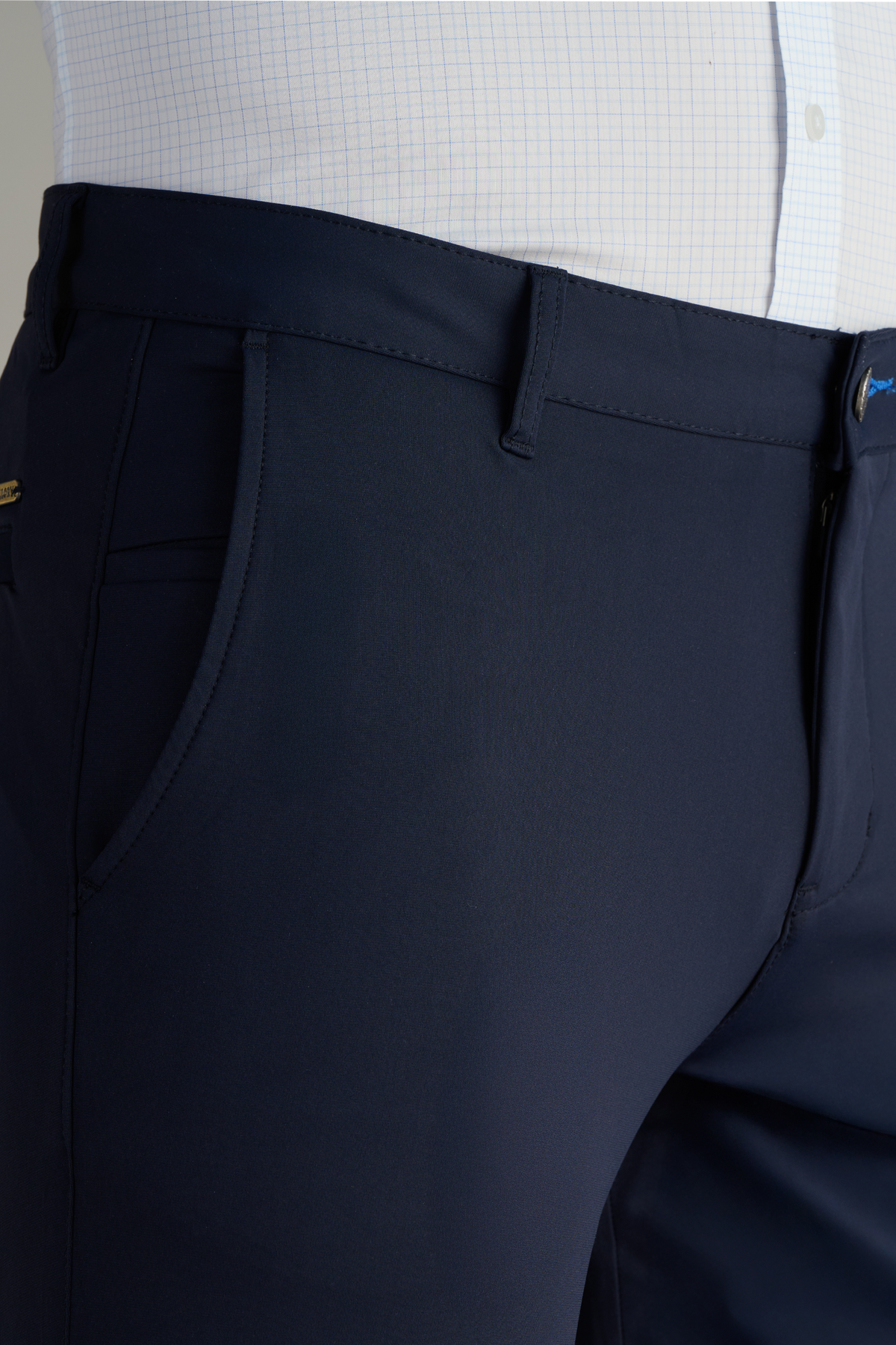 A close-up of Twillory Performance Pants // NAVY BLUE showcases the front pocket, neat stitching, and waistband with belt loop, paired with a partially visible white dress shirt featuring a faint grid pattern.