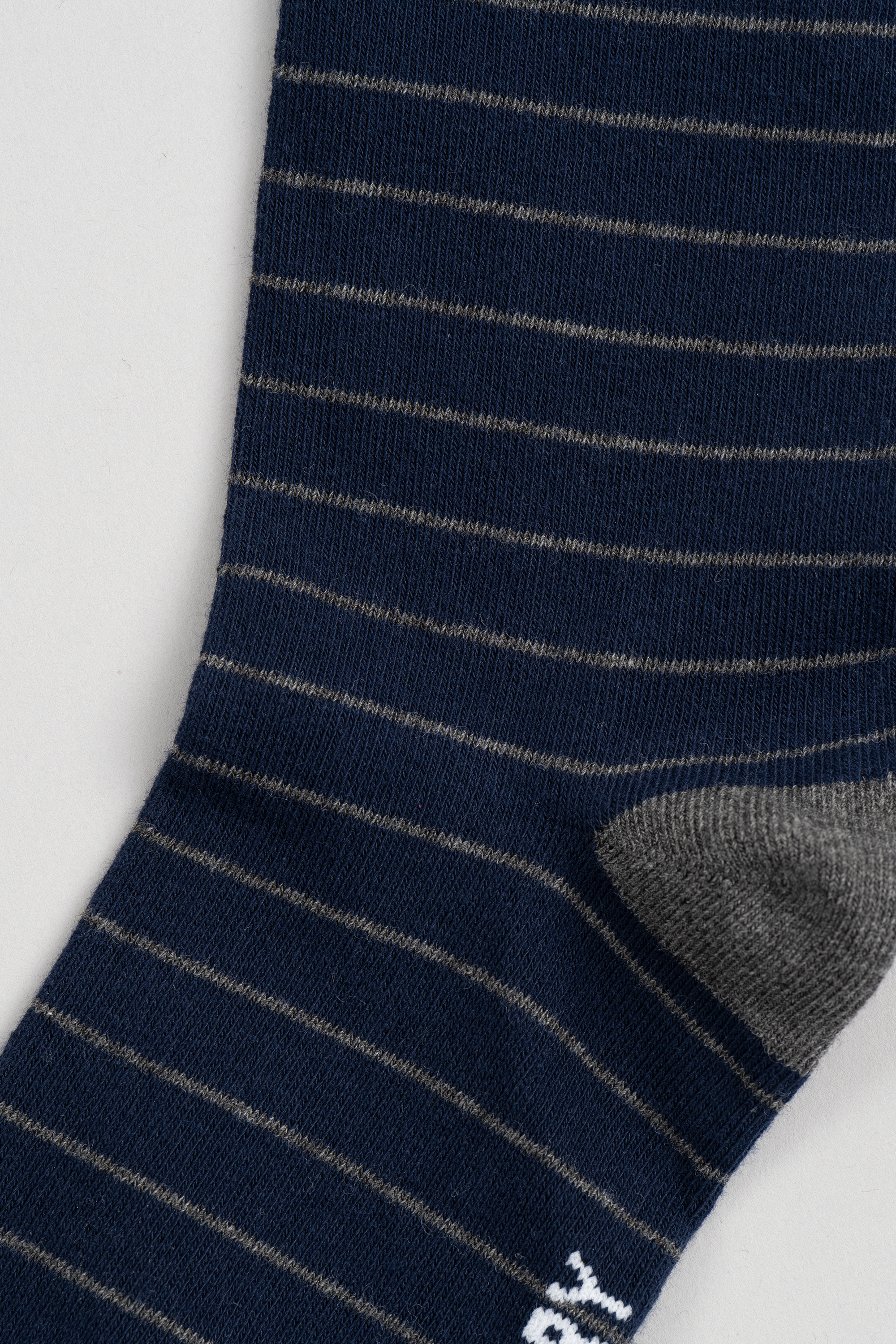 Close-up of the Twillory Navy Stripe sock, featuring thin light gray stripes on navy, a solid gray heel, and part of a white logo near the bottom left edge—all set against a plain light background. Discover your next favorite pair.