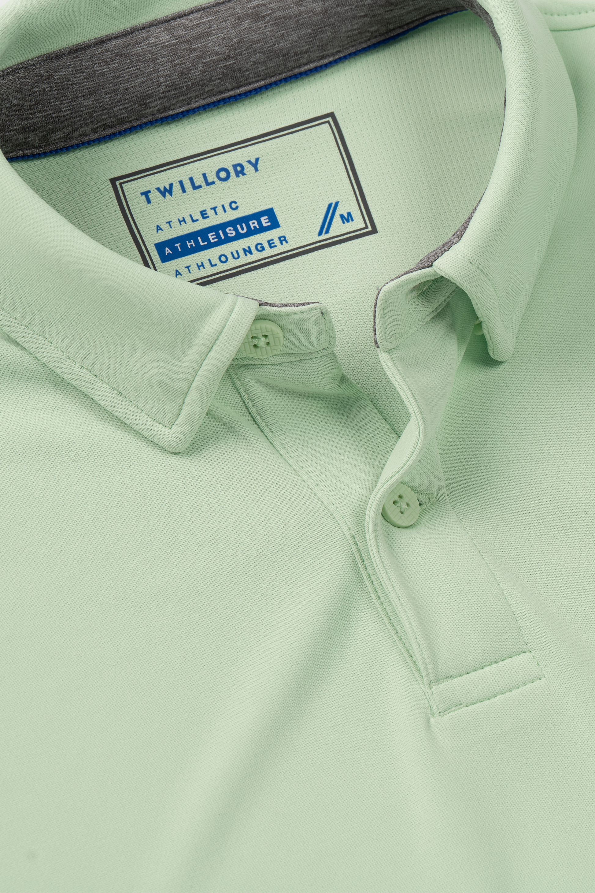 A close-up of the Twillory Short Sleeve Polo Solid in Pastel Green, featuring a soft collar, two buttons, gray lining, and Cooling Tech for all-day comfort. The inside label displays: "TWILLORY ATHLETIC ATHLEISURE ATHLOUNGER.