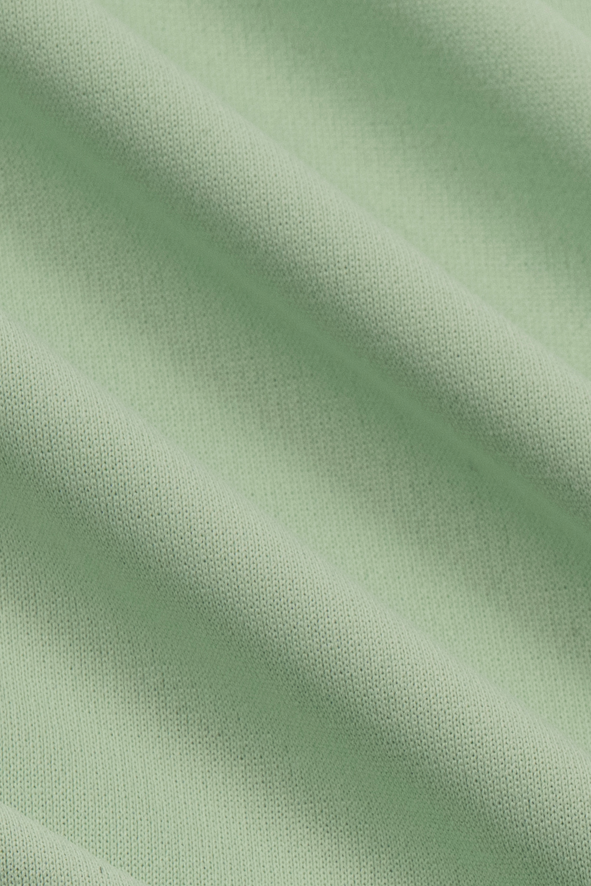 Close-up of pastel green fabric from the Twillory Short Sleeve Polo Solid, highlighting its fine knit texture, soft folds, and smooth, slightly stretchy material with cooling tech for comfort.