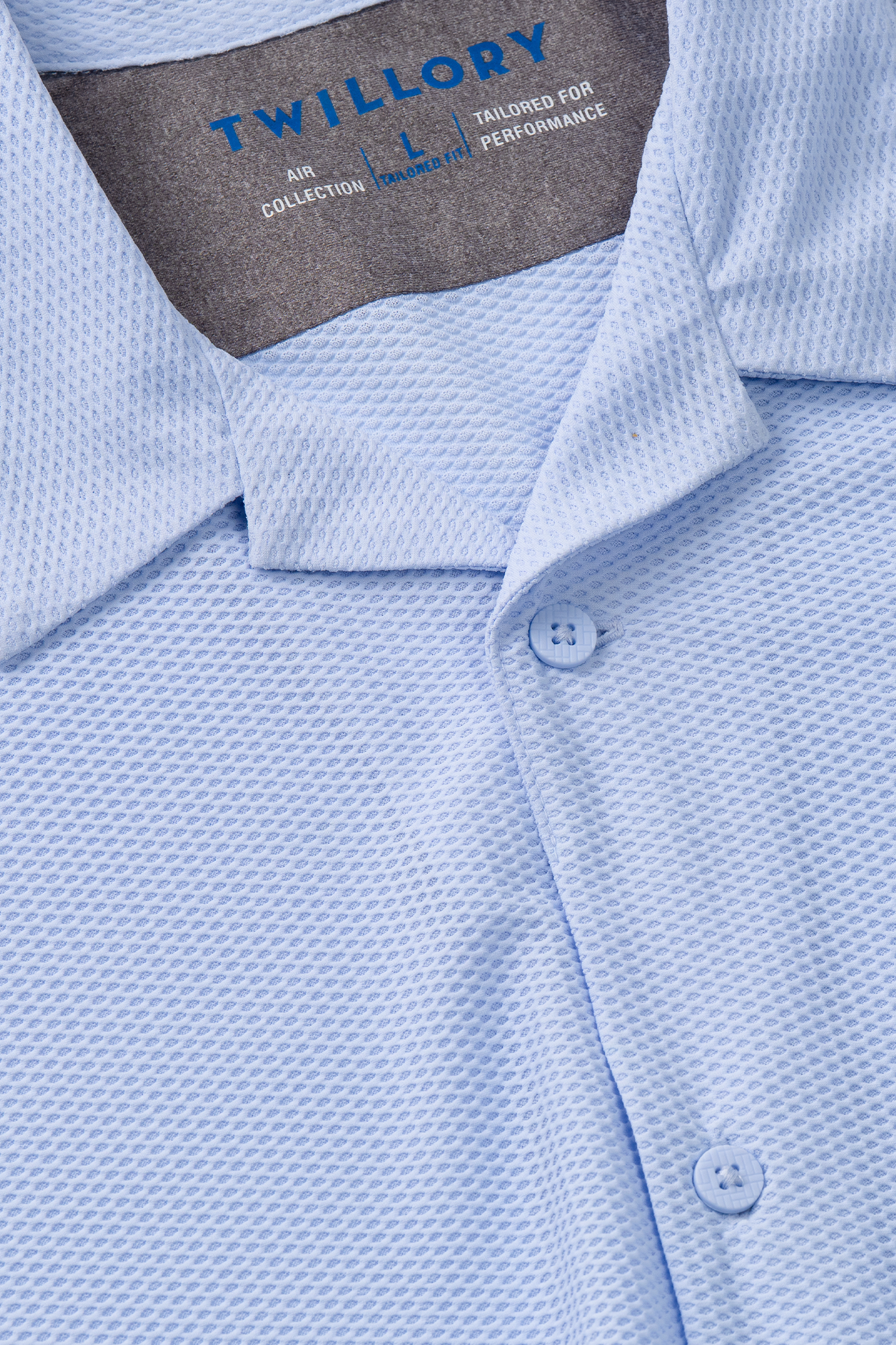Close-up of the Twillory AIR Resort Shirt Solid in Powder Blue, featuring cooling AIR fabric with a subtle waffle-like texture, collar, three buttons, and an inside label reading TWILLORY AIR COLLECTION L TAILORED FOR PERFORMANCE.